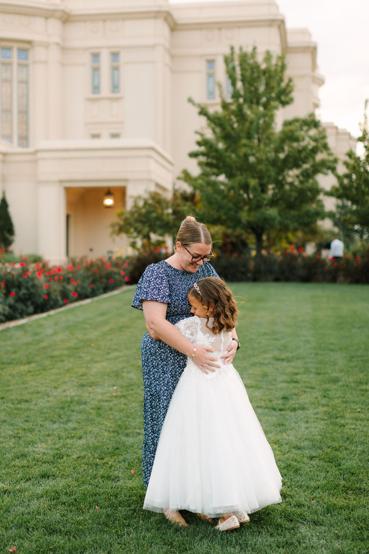 A heartwarming moment captured on a grassy lawn in front of a grand white building with rose bushes.