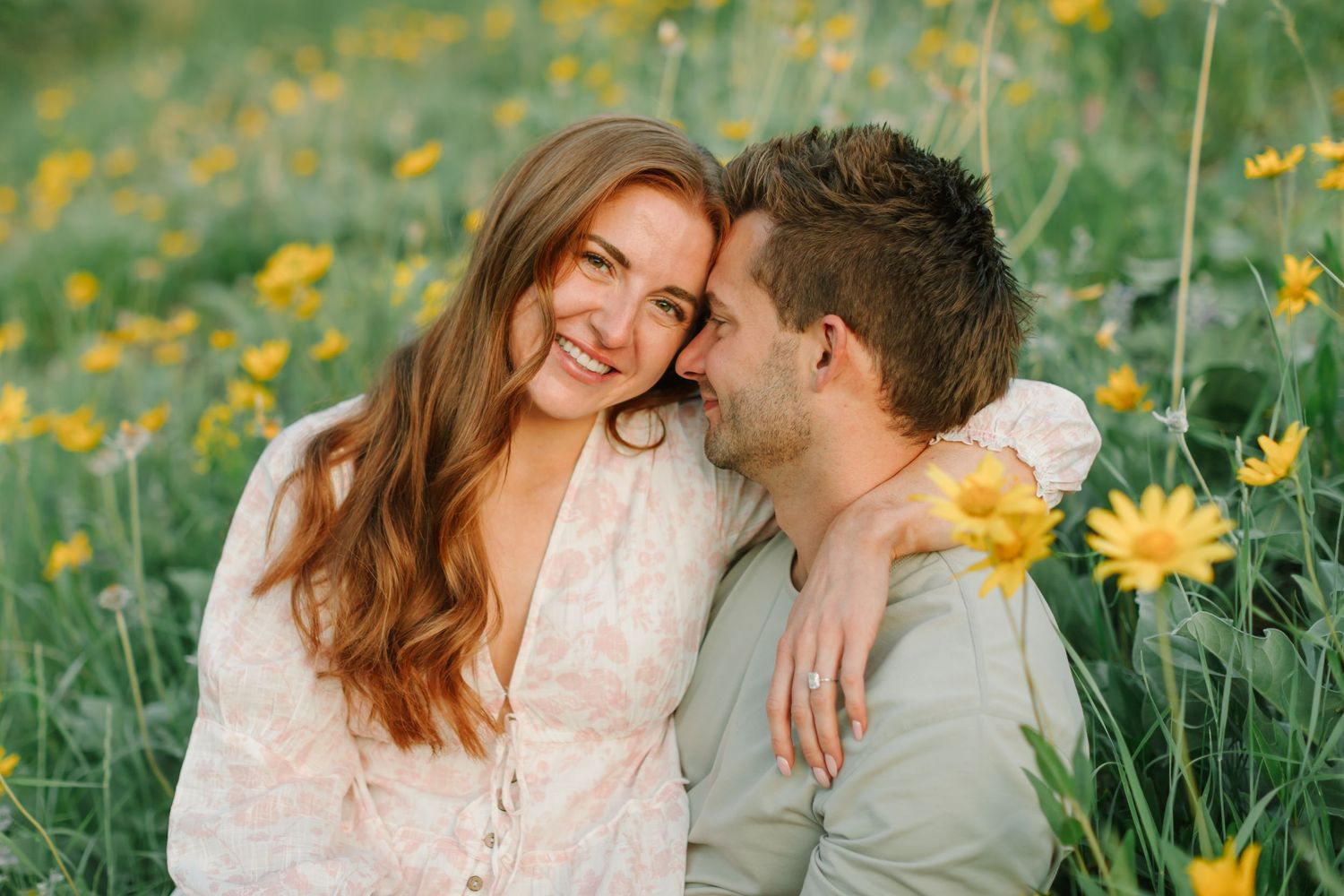 A couple shares a tender moment in a field of yellow wildflowers during a sunny outdoor photo session.