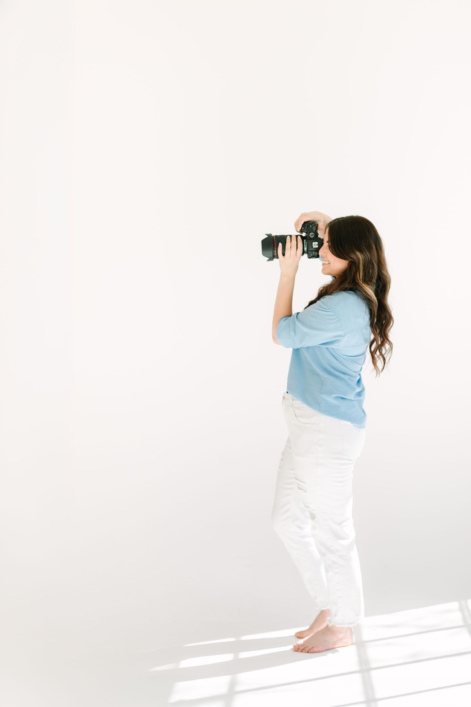 A photographer in a light blue shirt and white pants takes photos against a white background.