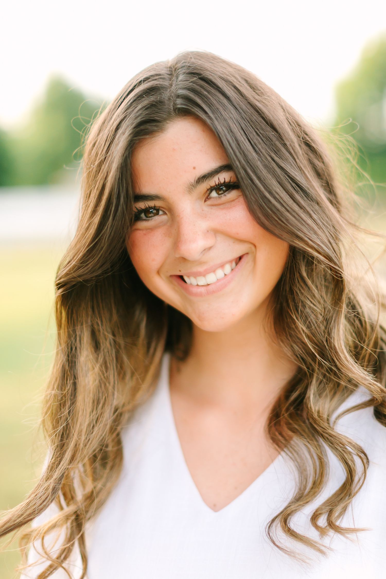 Portrait series showing wavy brown hair and white top against soft outdoor background.