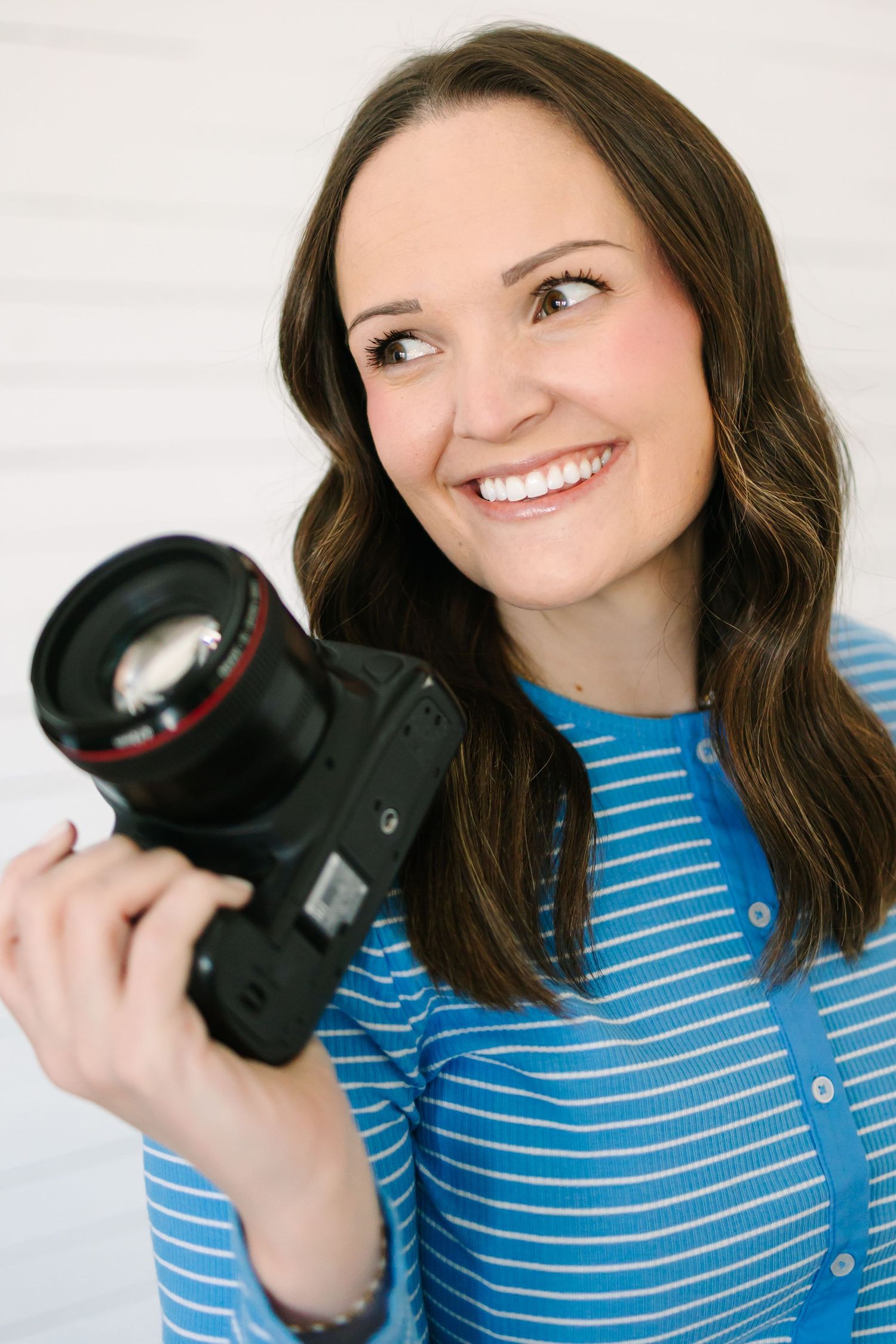A photographer in a blue striped shirt holds a DSLR camera while posing in a series of playful expressions.