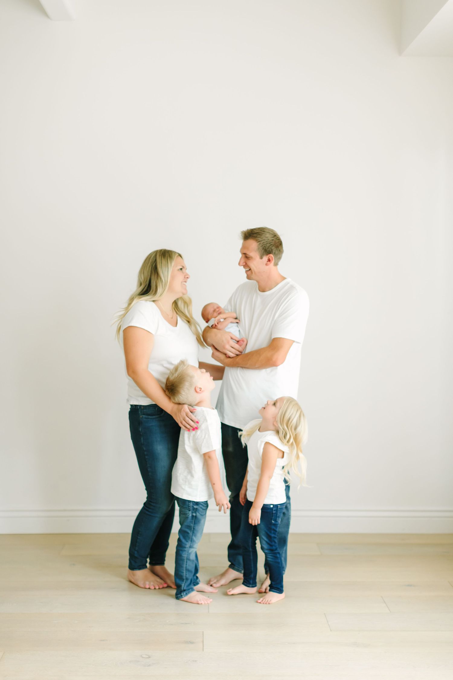 A family of five stands together in a minimalist white room wearing casual clothing.