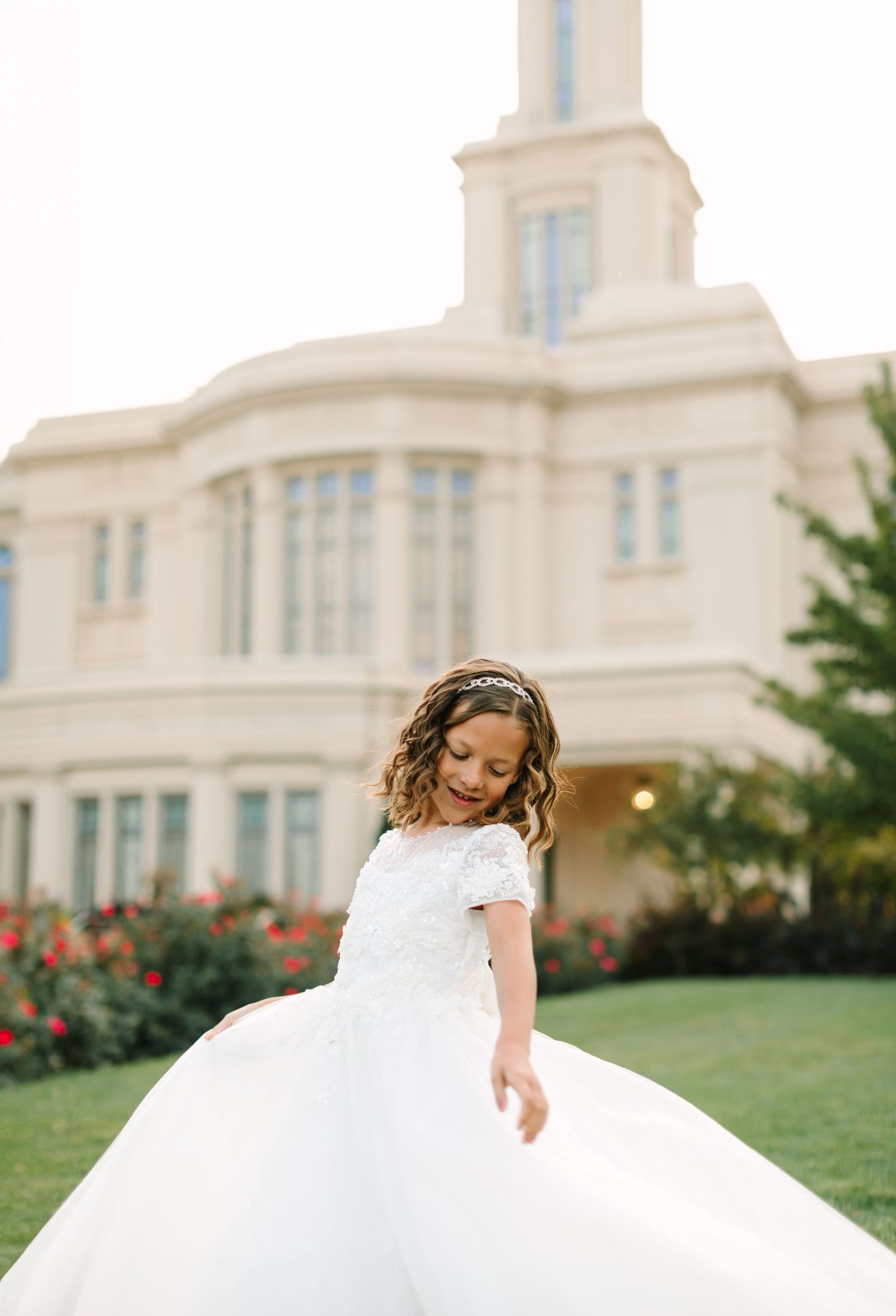 A young girl in a white dress twirls joyfully on a grassy lawn in front of a grand white building.
