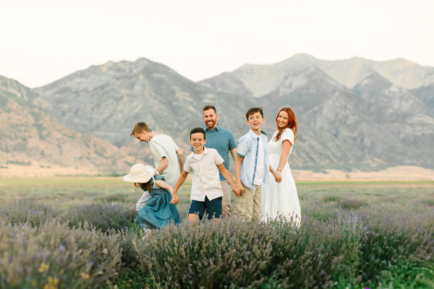 A group sits together on a grassy hillside overlooking scenic mountain ranges in the distance at sunset.