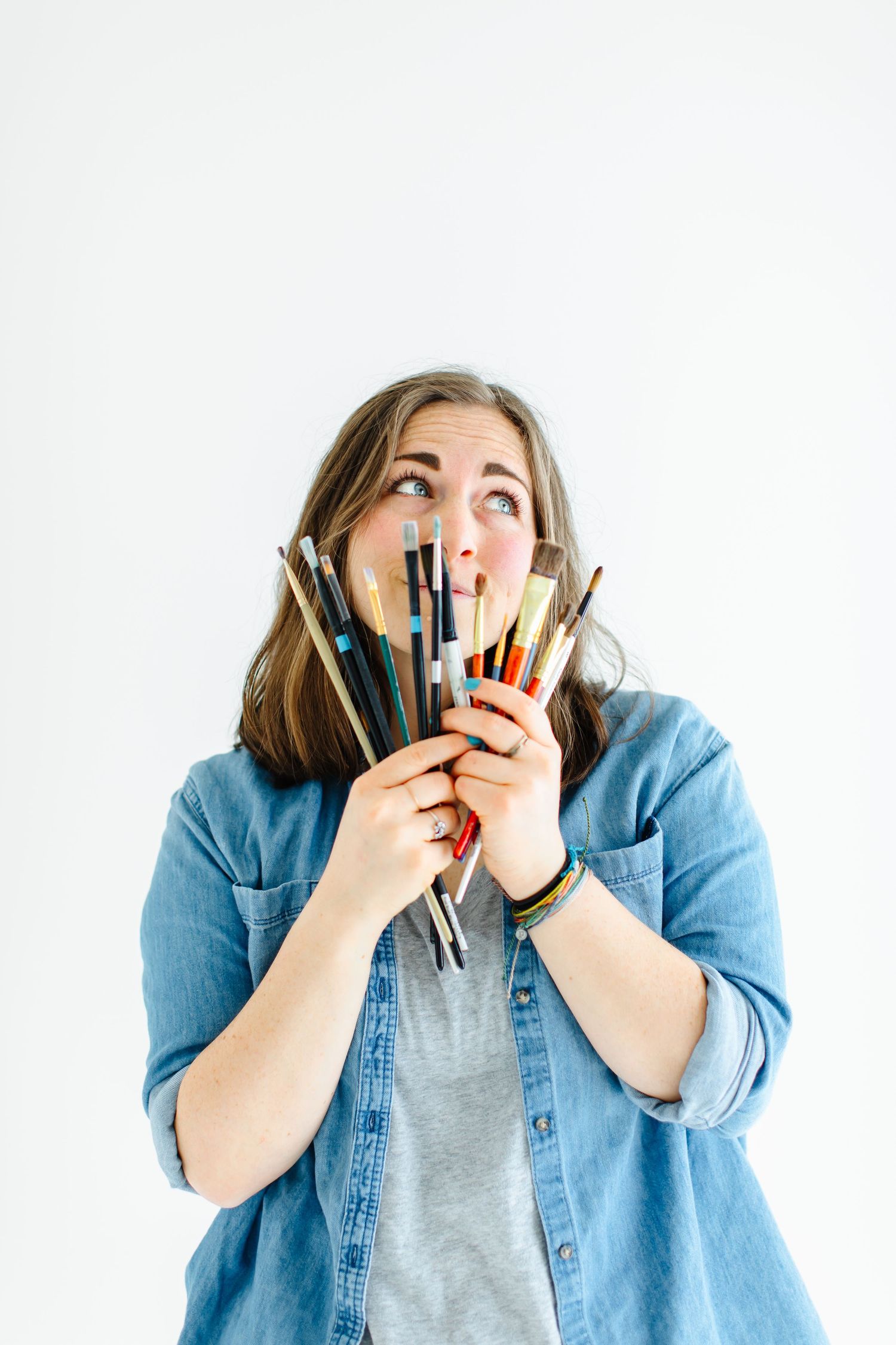 Artist playfully holds bundle of art brushes and pencils near face at White Space Studios in Provo, Utah in Utah County..