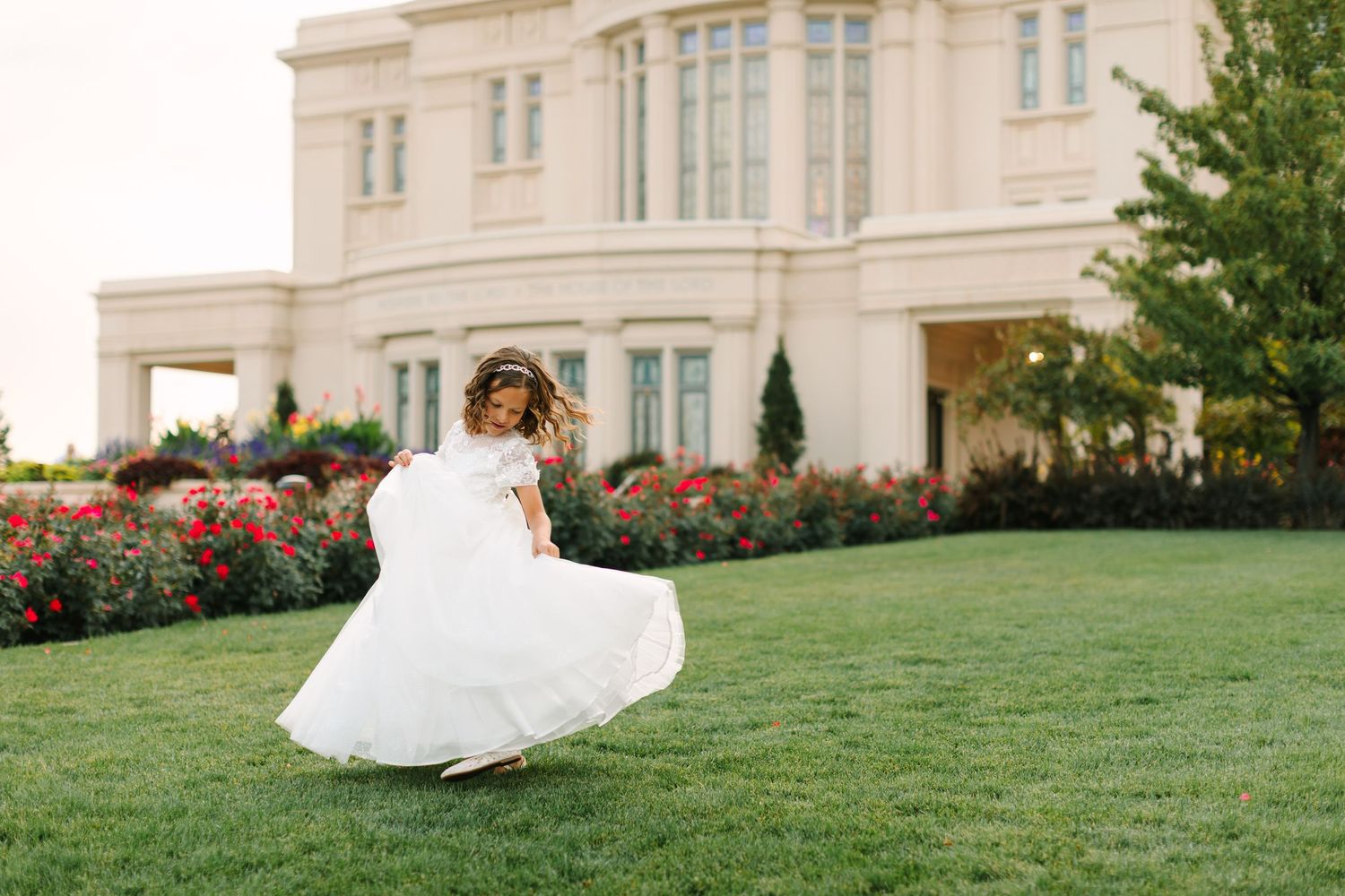 A flowing white wedding dress twirls gracefully on a manicured lawn with an elegant mansion in the background.