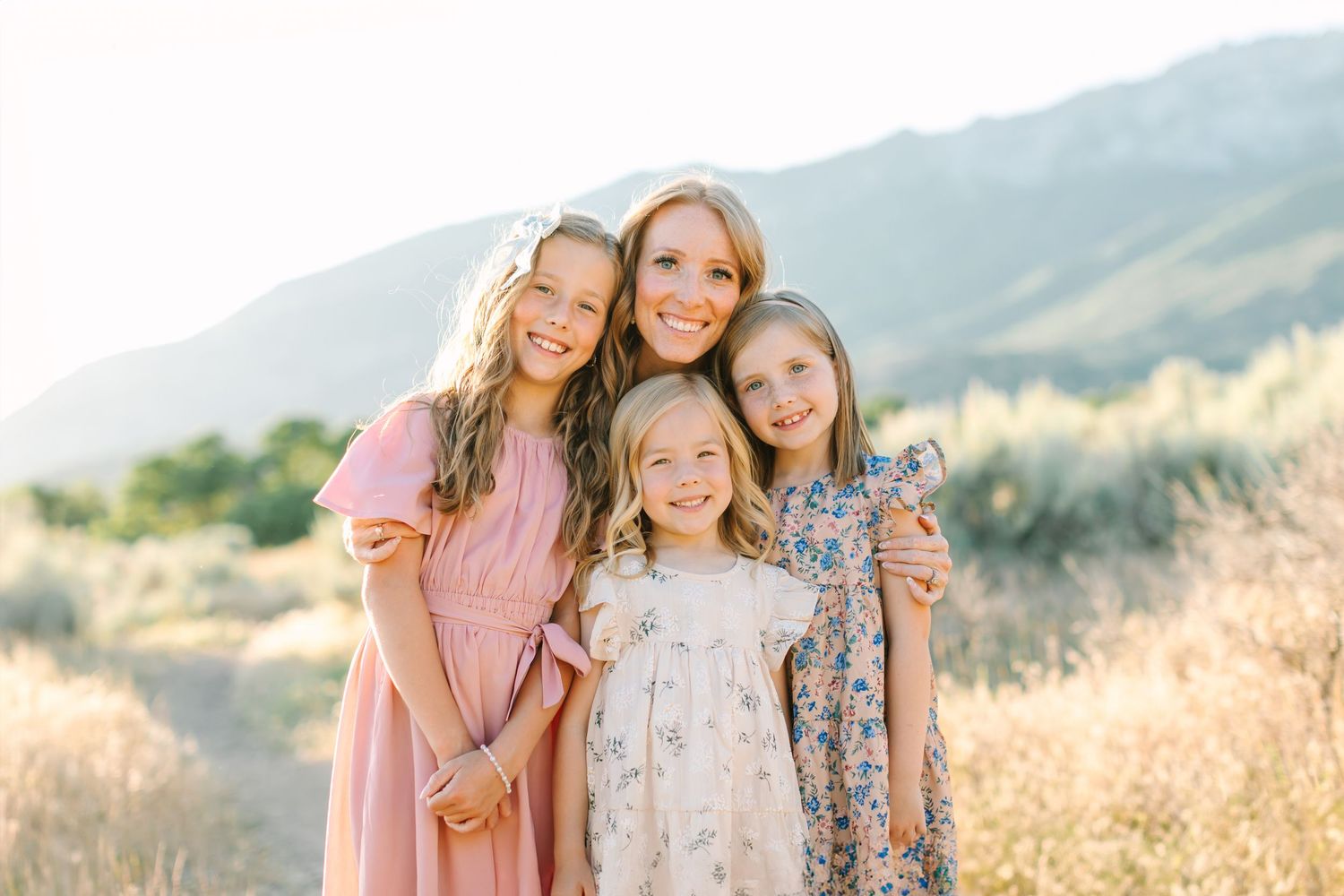 Three people wearing coordinating outfits pose together in a golden field with mountains in the background at sunset.