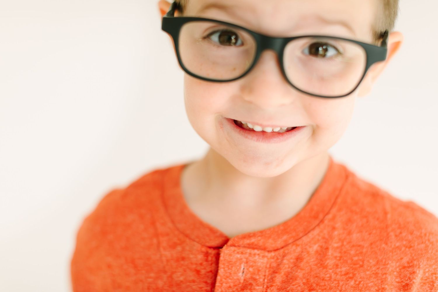 A person wearing black-framed glasses smiles brightly against a white background in a series of four photos.