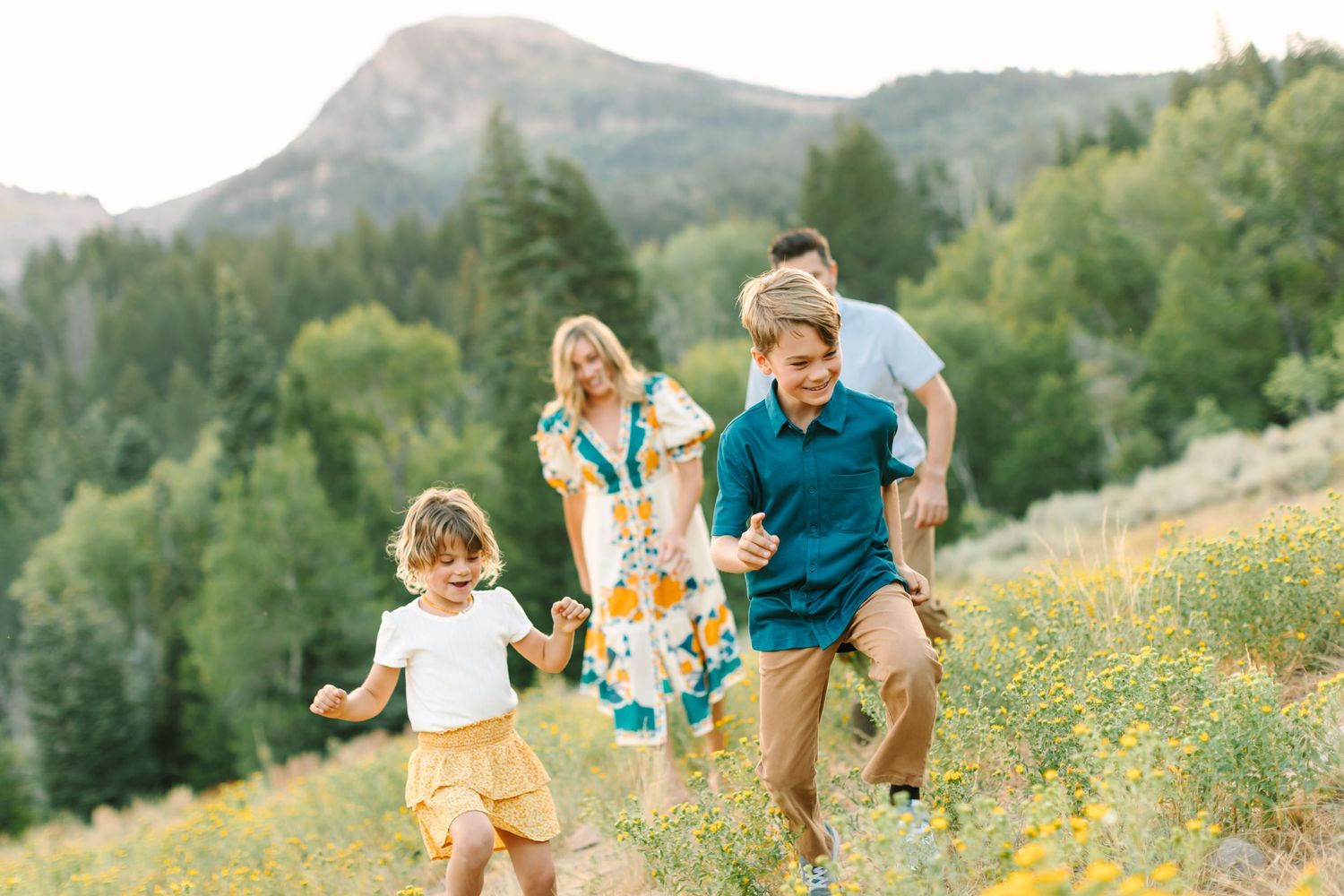 Family in colorful outfits runs and plays together through a wildflower-filled mountain meadow on a sunny summer day.