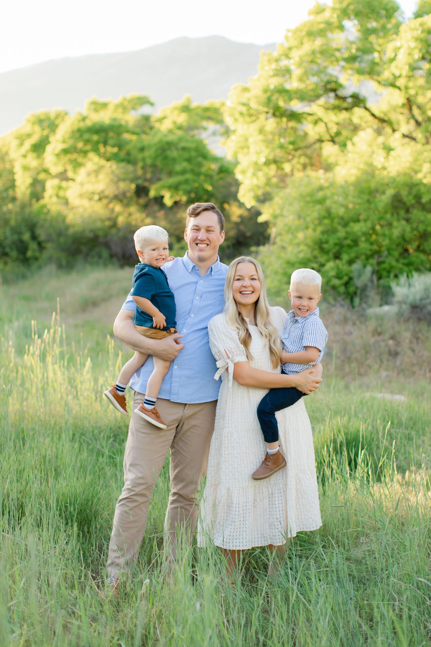 A family shares joyful moments together in a sunlit meadow with tall grass and trees in the background.