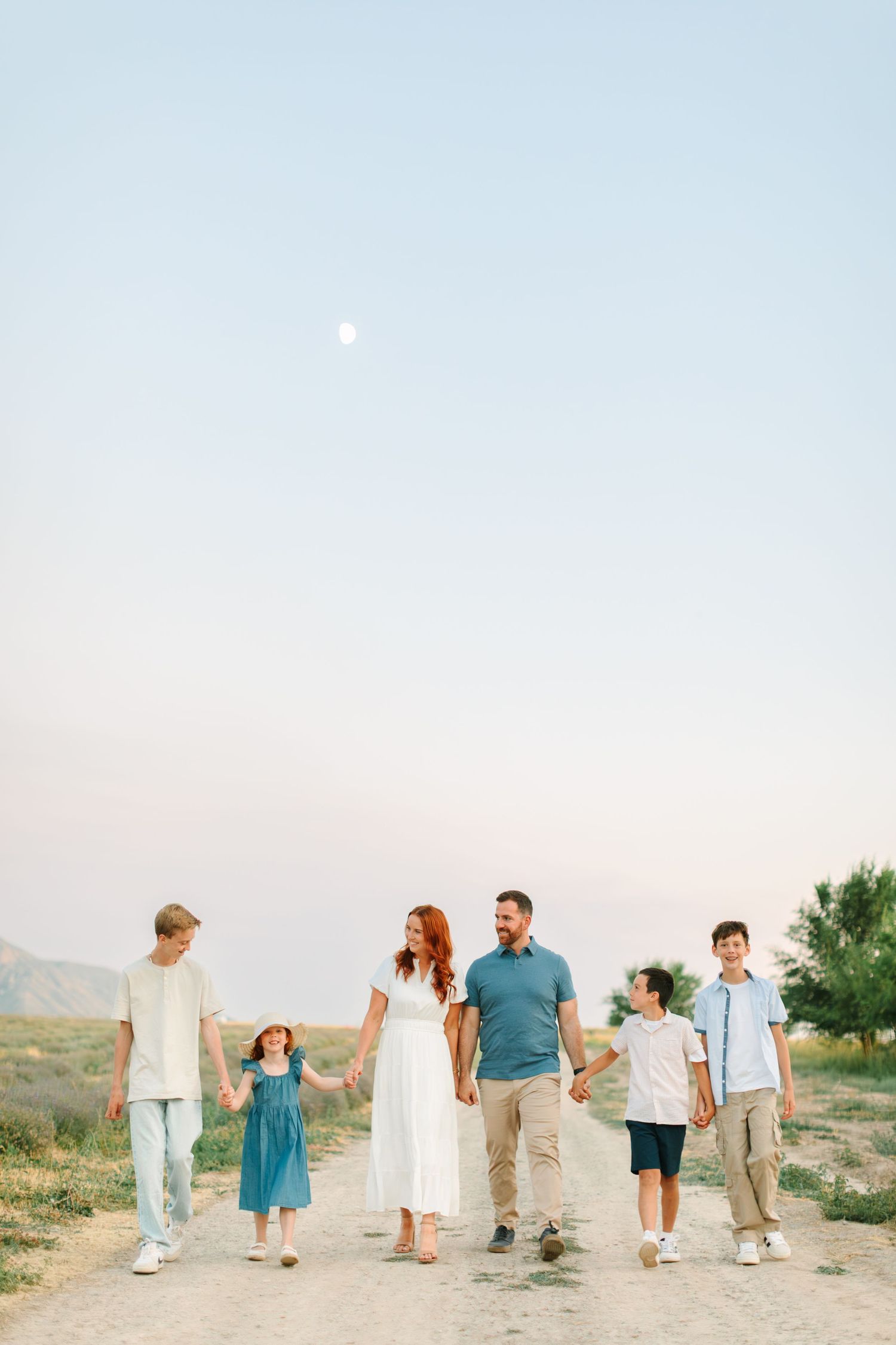 People walking together along a desert path with mountains in the background during sunset.