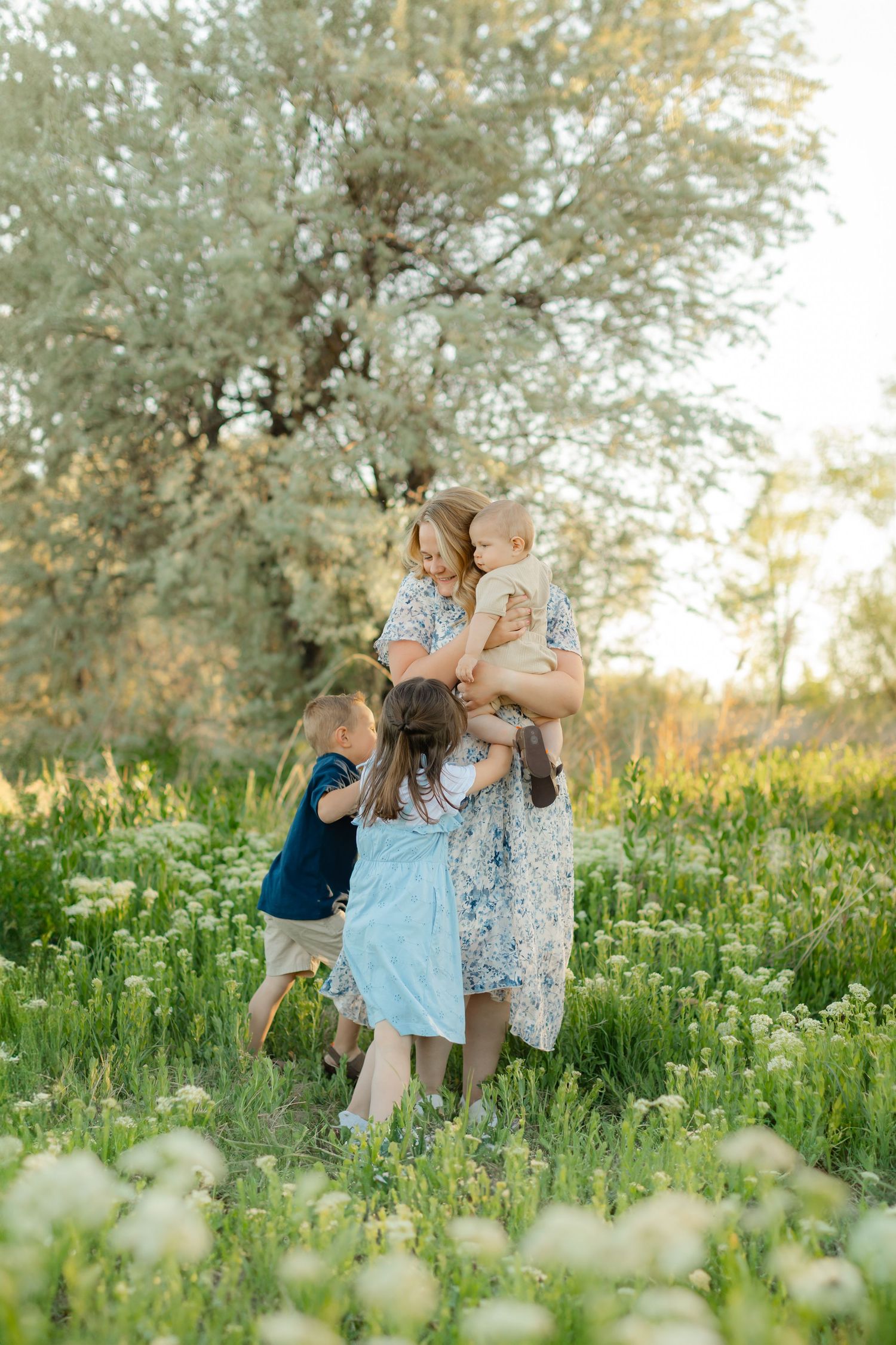 Family plays together in a wildflower meadow at sunset surrounded by white blooms and olive trees.