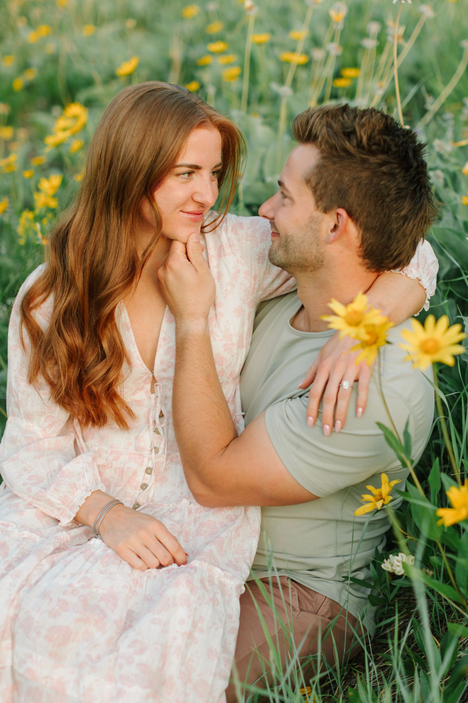 Romantic couple sharing tender moments while sitting in a blooming wildflower meadow on a sunny day.