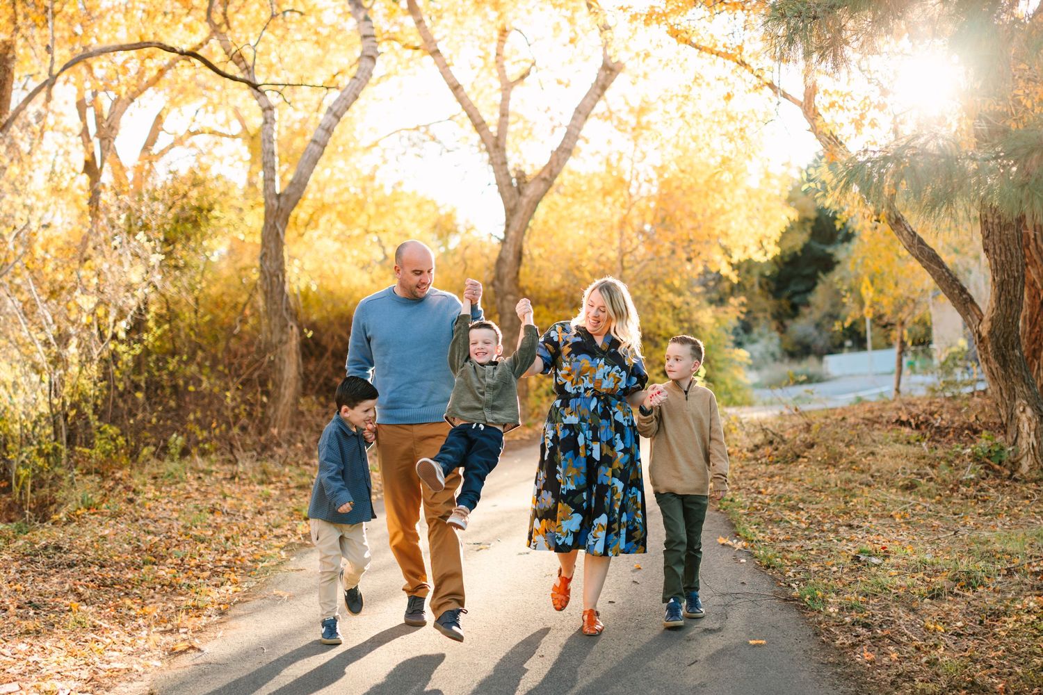 A family walks together on a path during golden hour with autumn trees and sunlight creating a warm atmosphere.