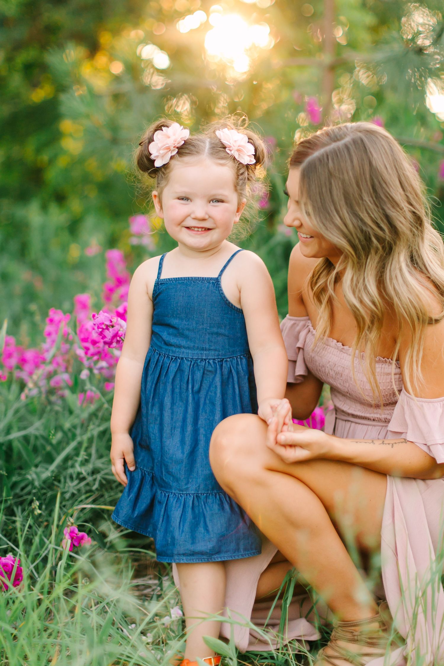A heartwarming outdoor photoshoot in a garden with pink flowers and golden sunlight filtering through the trees.