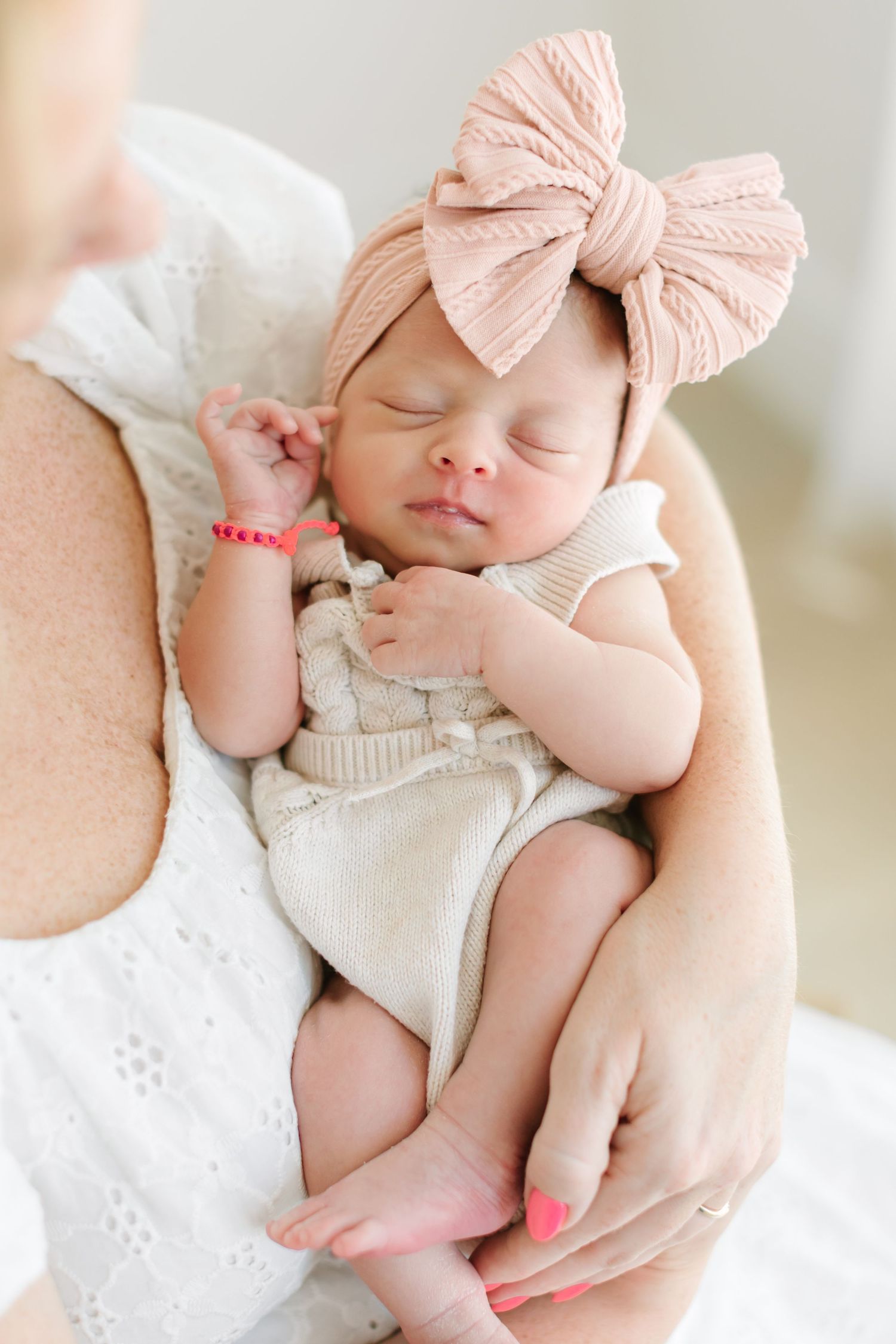 Sleeping baby in cream knit outfit with pink bow headband resting peacefully.