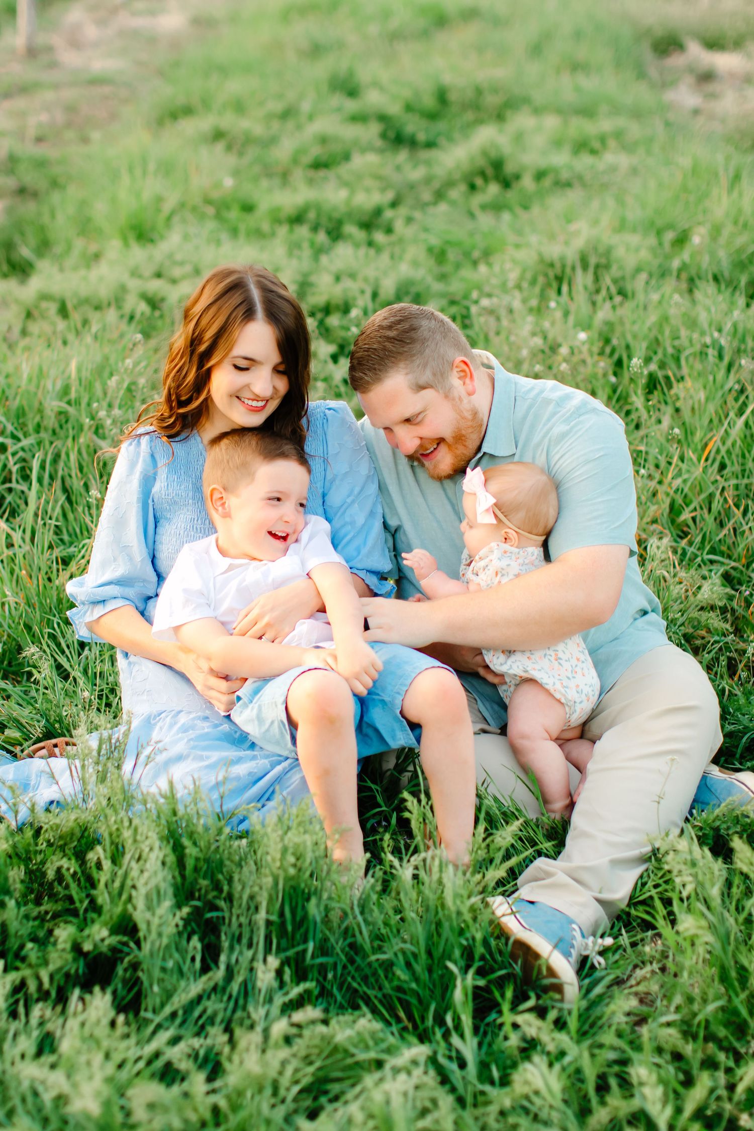 A family plays together in green grass at a blooming orchard for their family photoshoot in Santaquin, Utah.