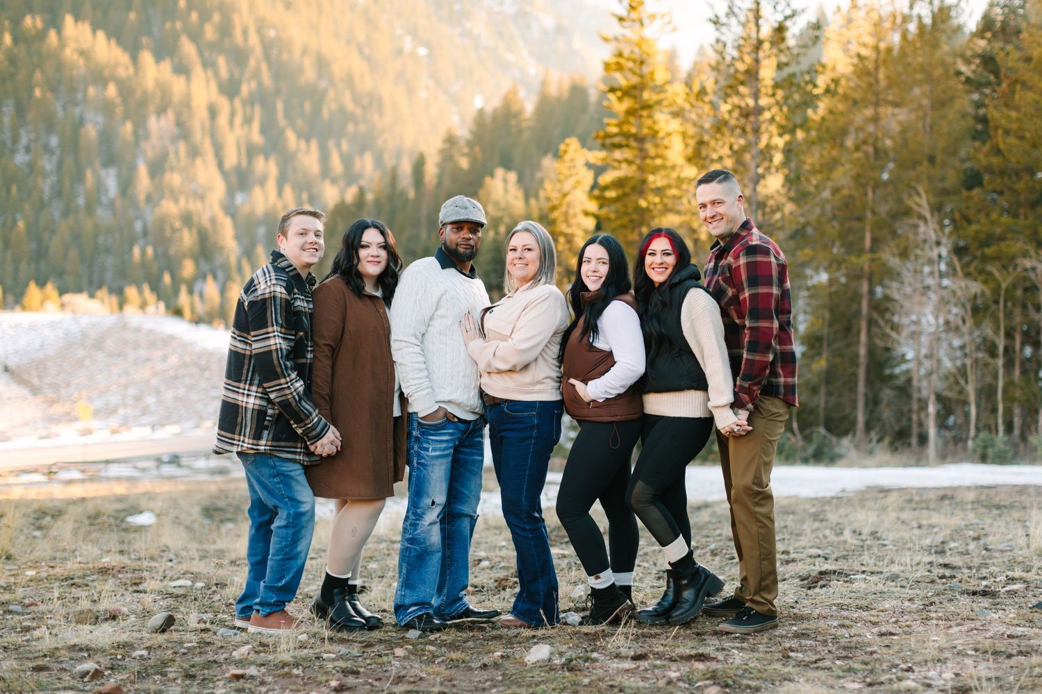 A group of people stand together outdoors during golden hour with evergreen trees in the background.