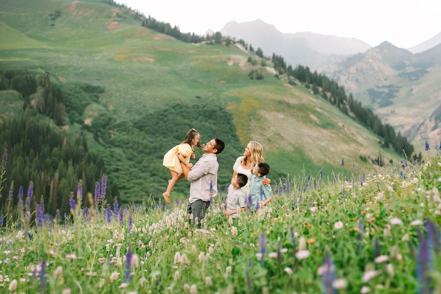 Family playing in a wildflower meadow with lush green mountains in the background on a sunny day.