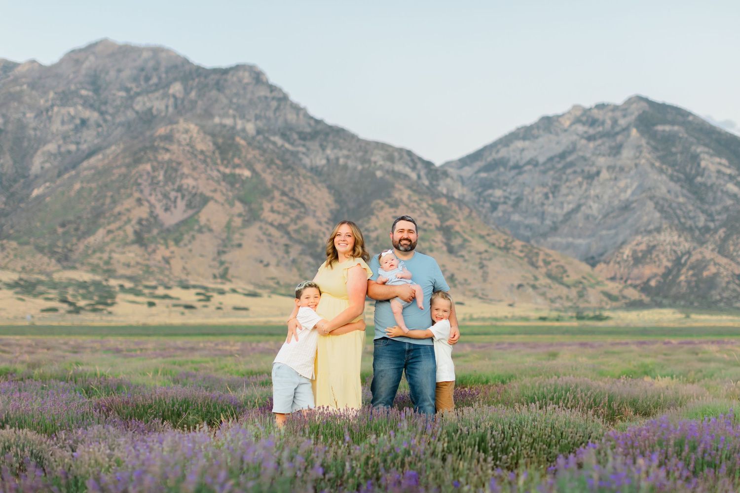 A group of people stand together in a field of purple wildflowers with scenic mountains in the background.