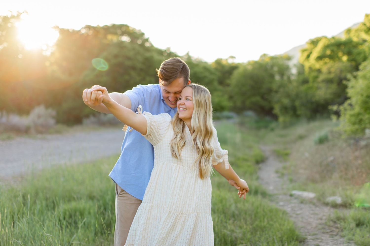 A couple dancing together on a dirt path at sunset with golden light filtering through trees in the background.