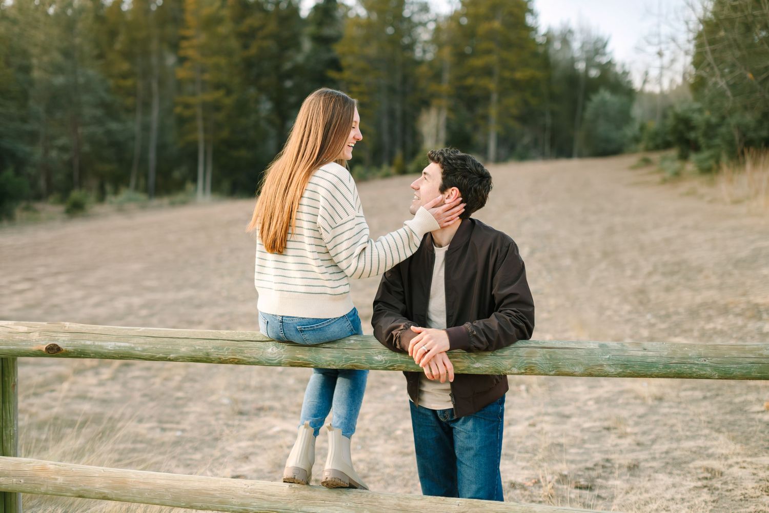 Two people sit close together on a grassy hillside during an engagement photoshoot in nature.