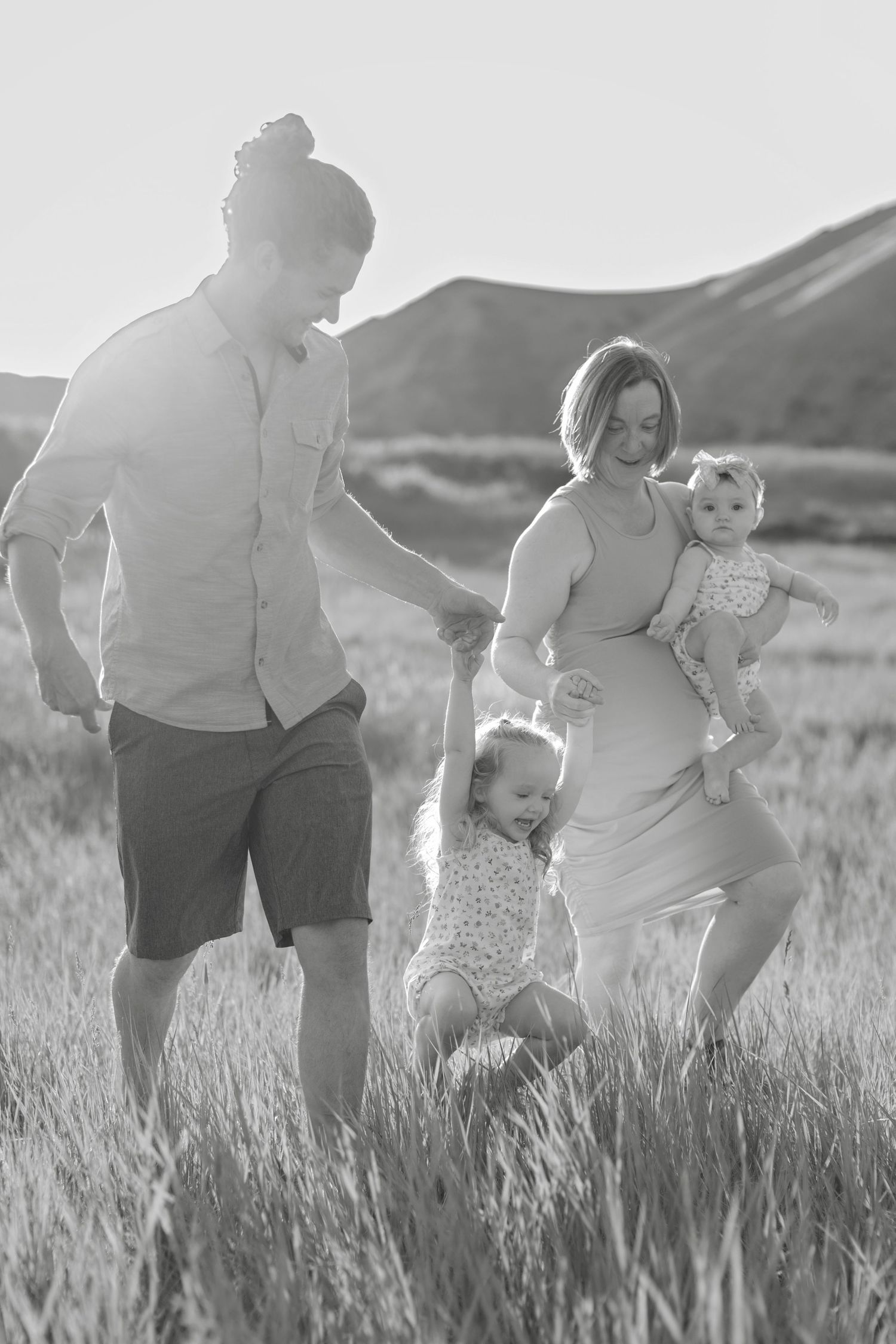 A family plays together in a grassy field during a black and white outdoor photoshoot.