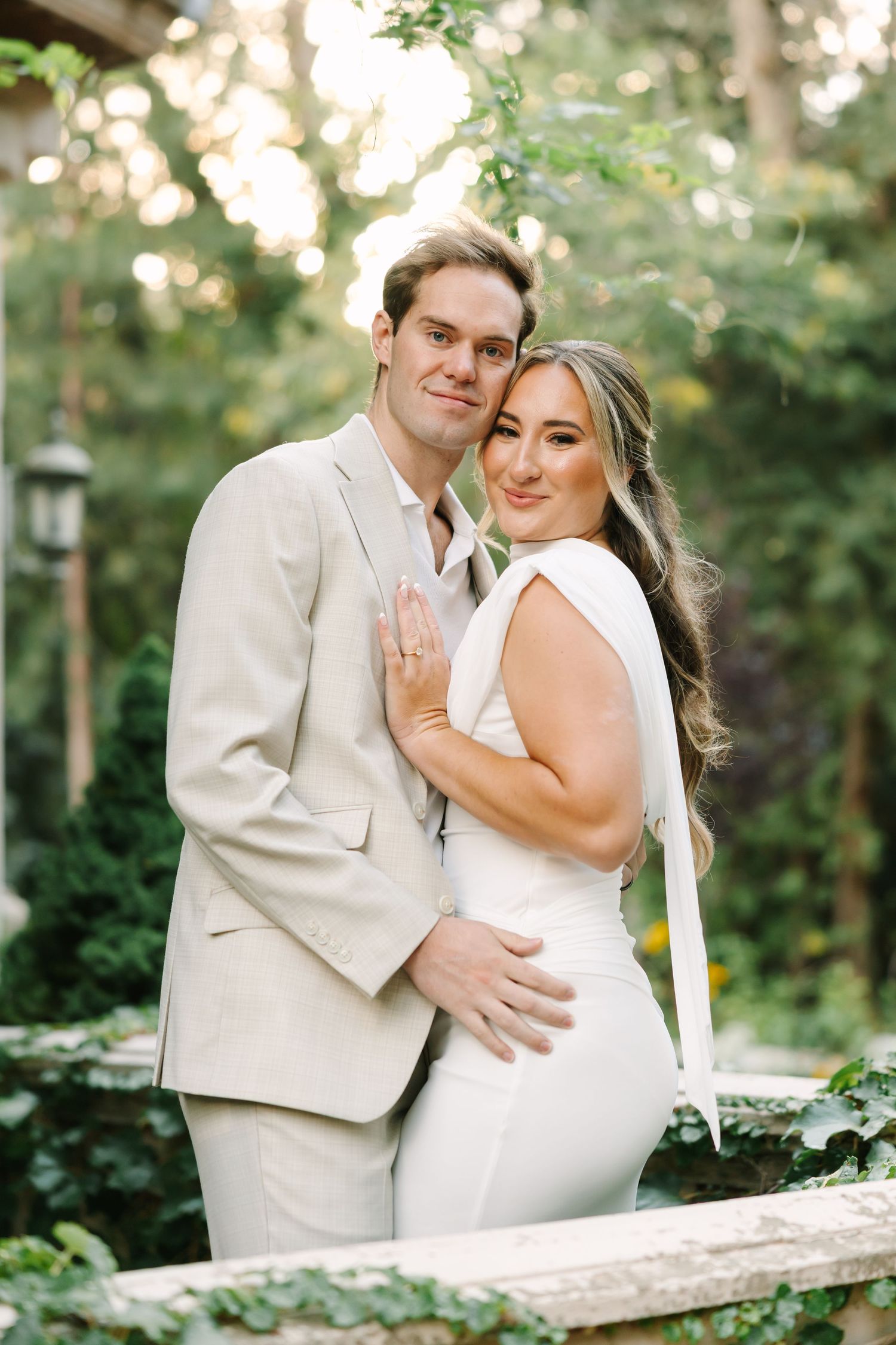 A couple shares a romantic moment in their wedding attire against a lush garden backdrop on their special day.
