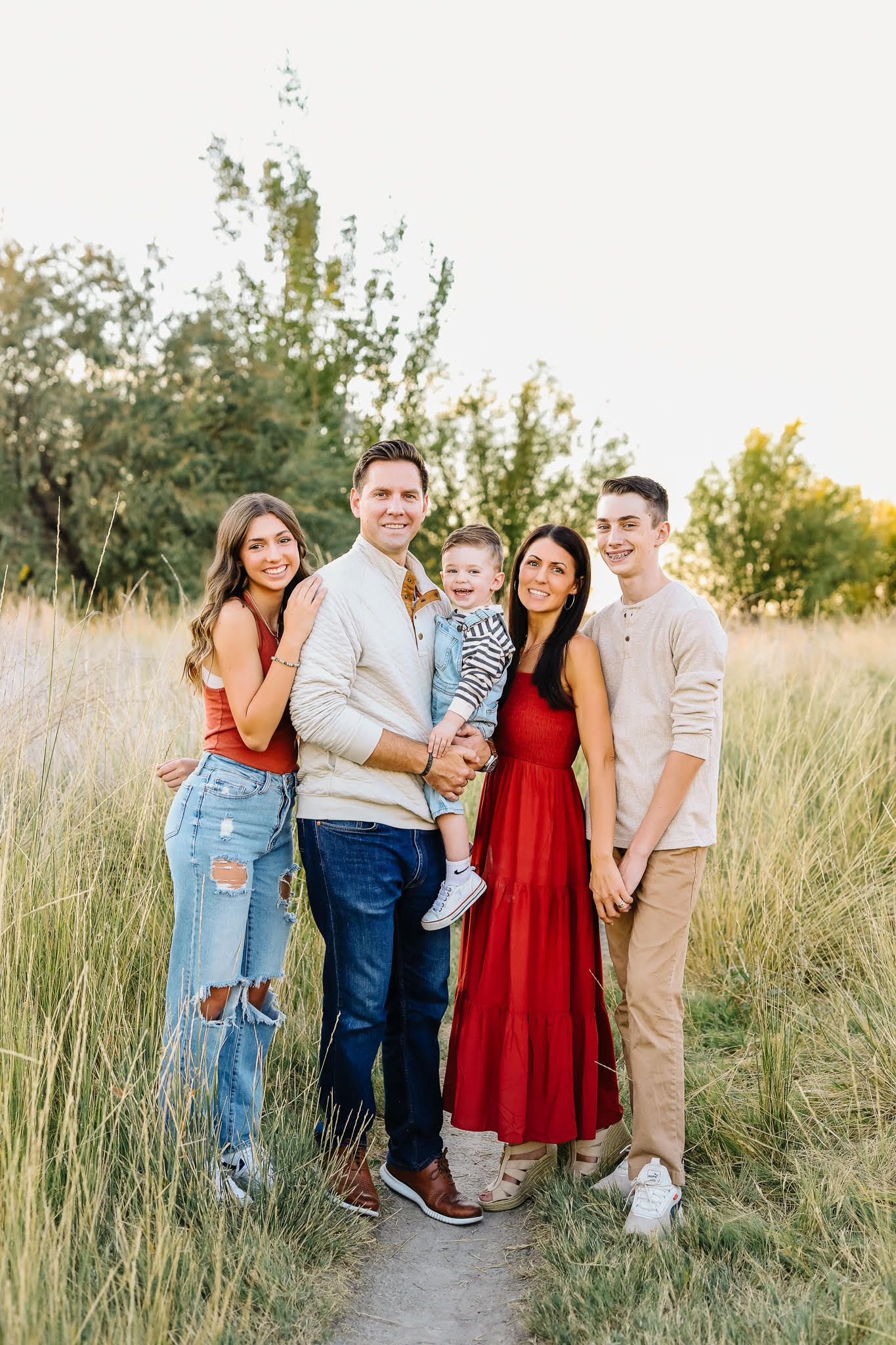 A group poses together in a grassy field during golden hour wearing coordinated casual and dressy outfits.