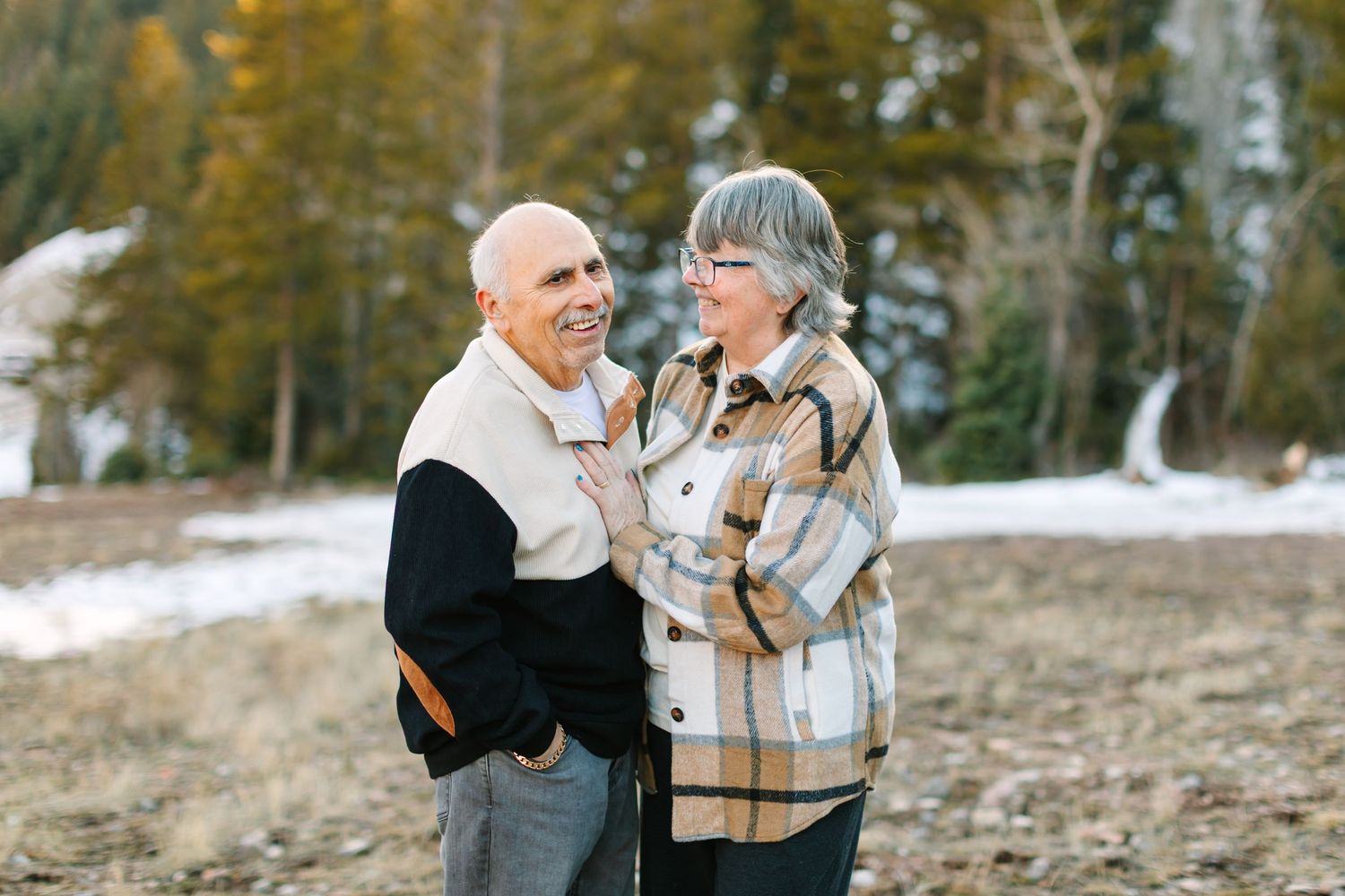 Couple embraces in front of snowy mountain landscape during winter engagement photoshoot.