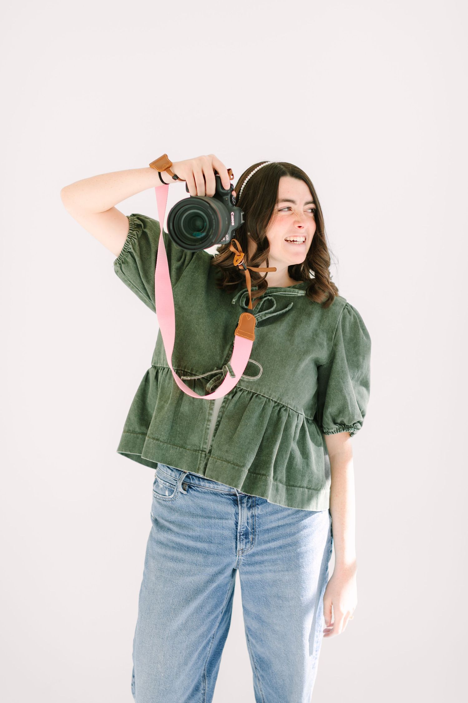 Person in olive green top and light wash jeans poses with vintage camera in three different playful stances.