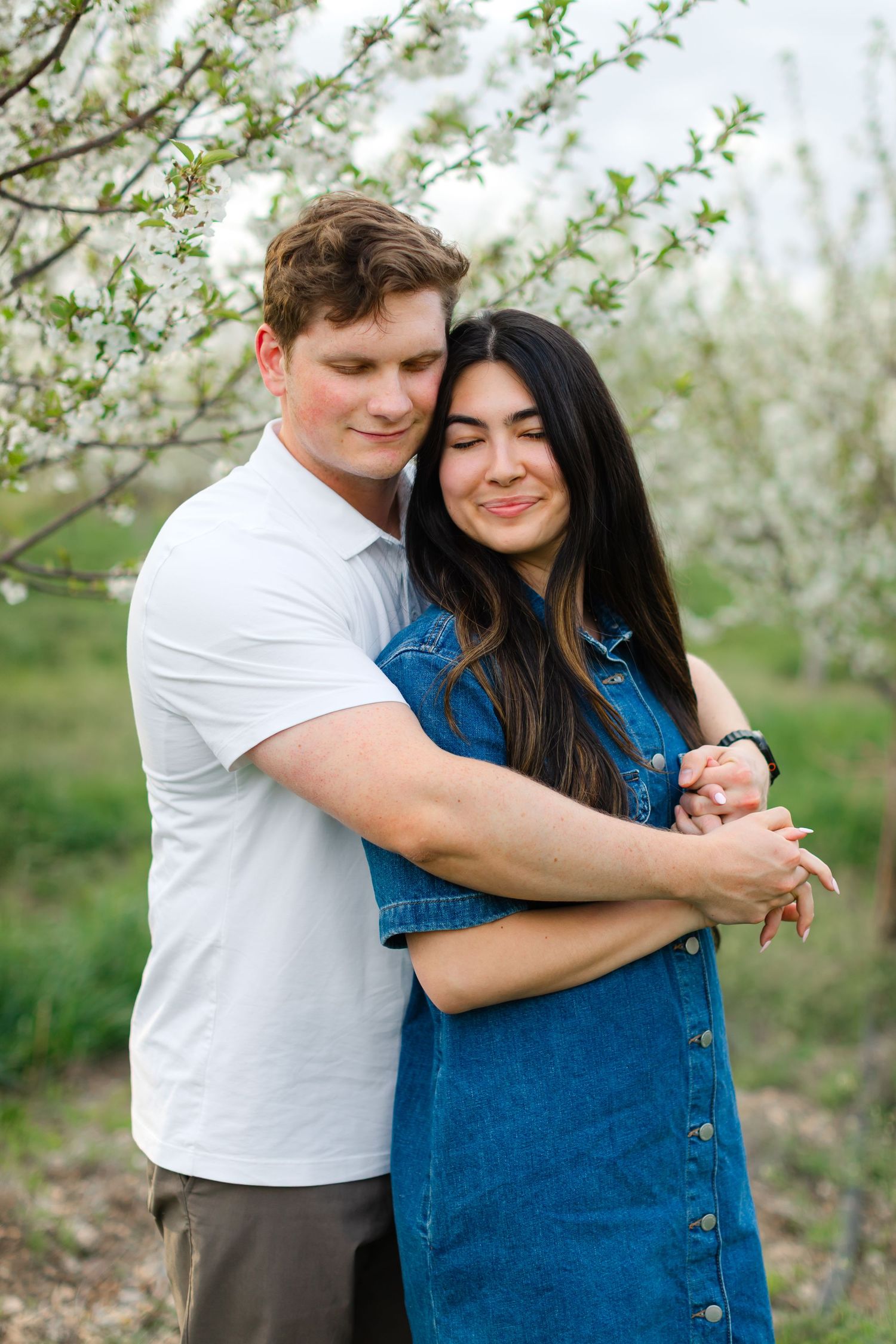 A couple shares tender moments in a spring orchard with blooming white flowers in the background.