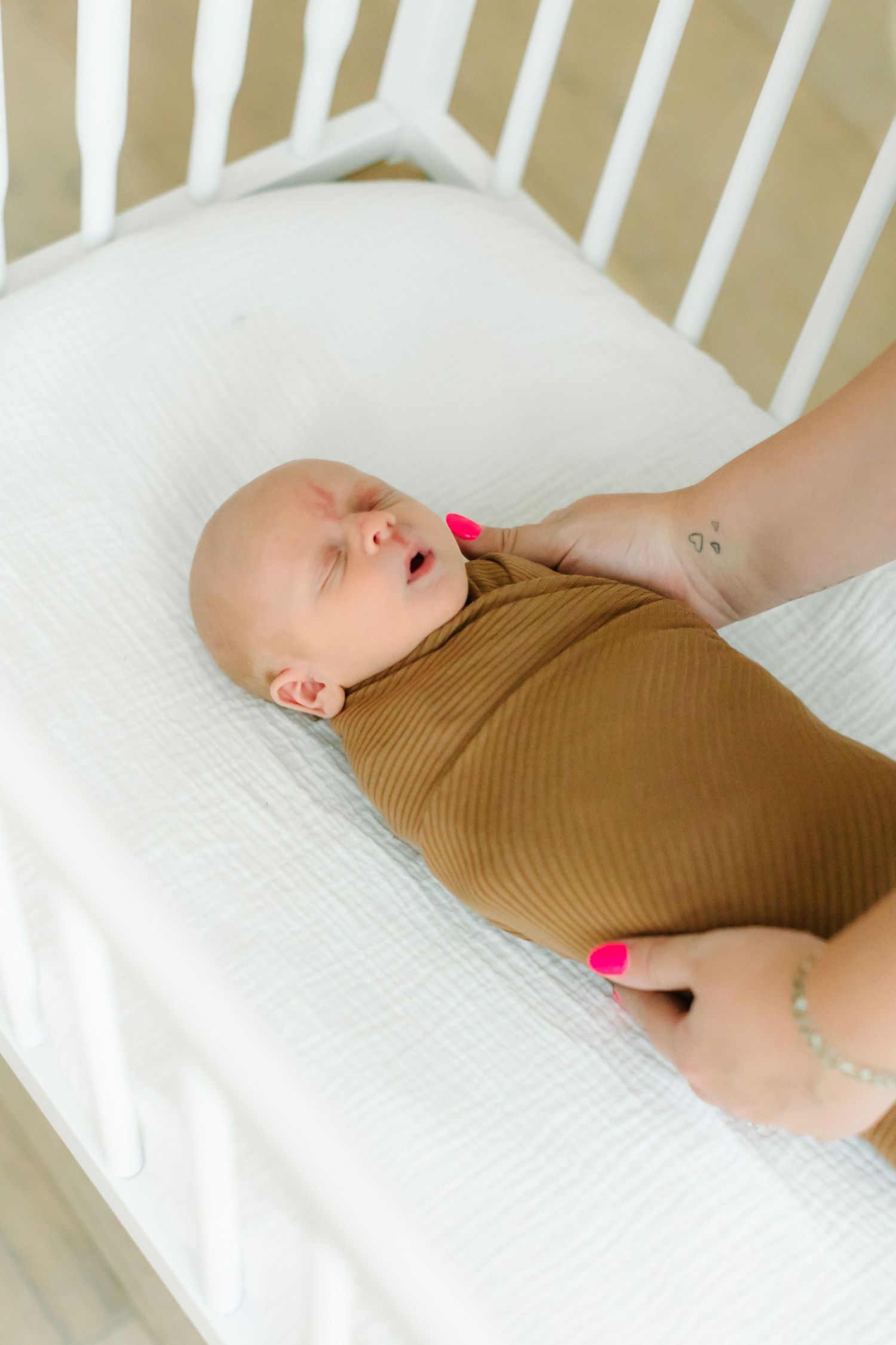 A sleeping baby in a brown onesie rests peacefully in a white crib.