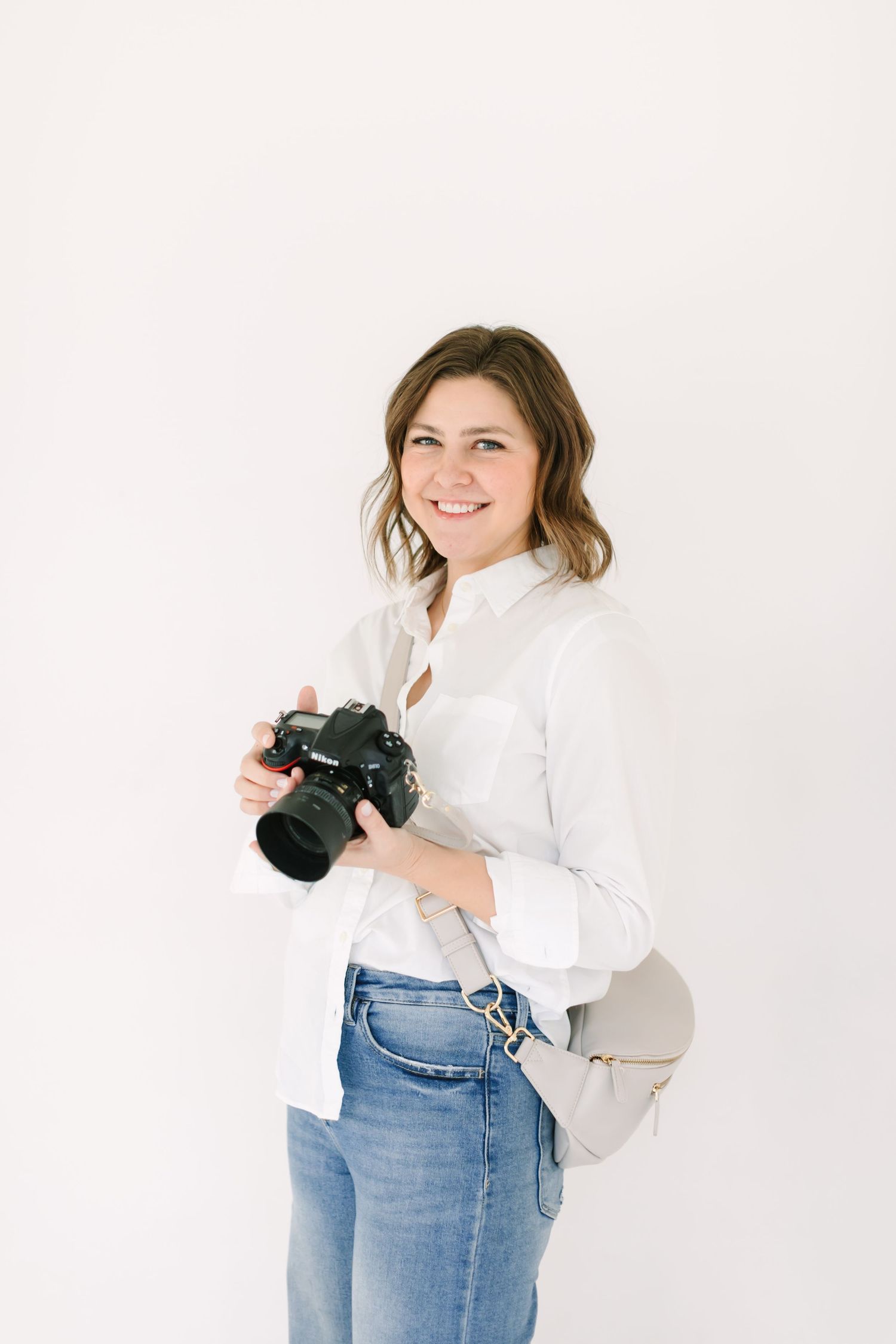Professional photographer in white shirt and jeans holds camera against white background in three poses.