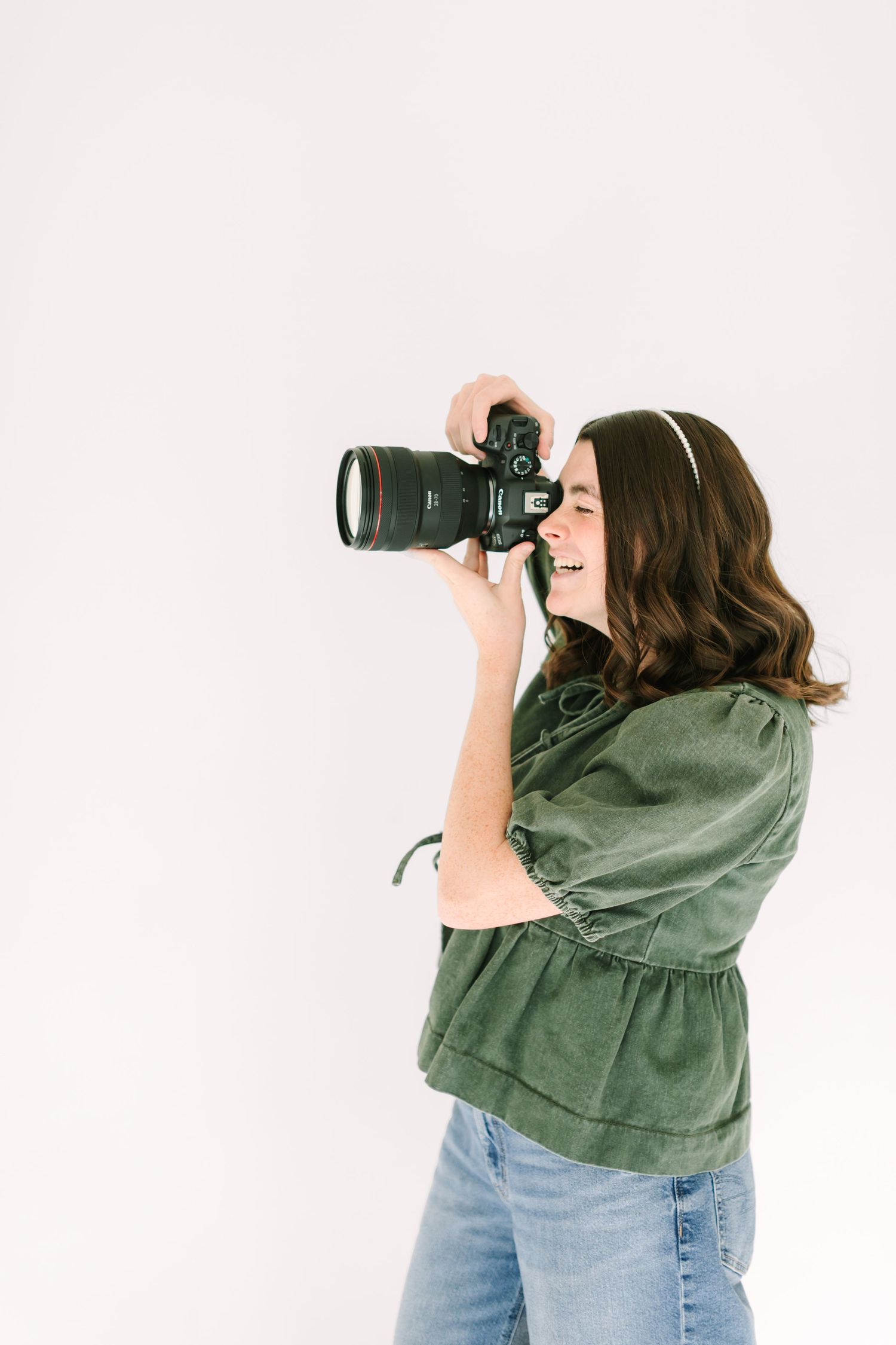 Photographer in green jacket and jeans using professional camera with telephoto lens against white background.