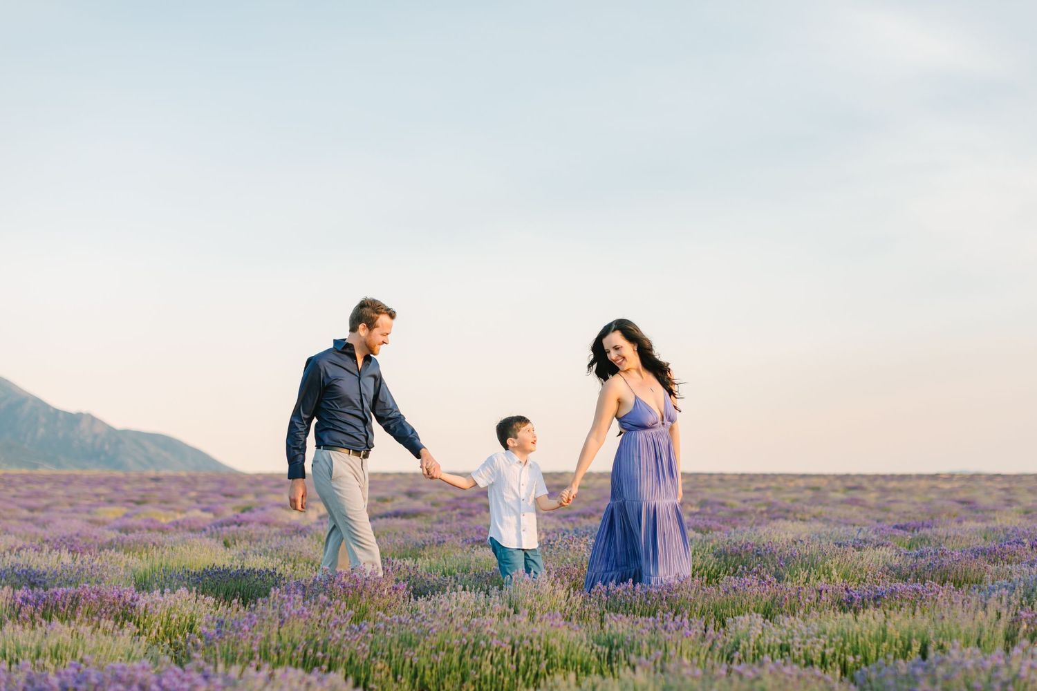 Family walking together through a beautiful purple lavender field at sunset with mountains in the background.