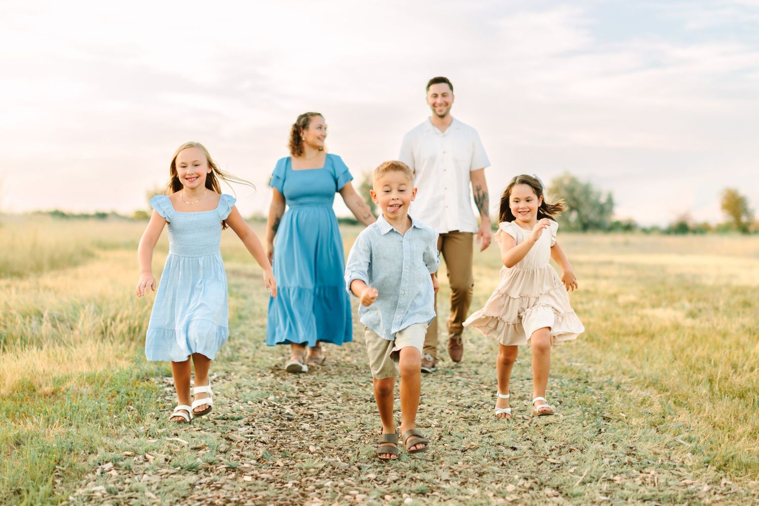 Happy family of five walking hand-in-hand through a sunny field, children laughing in blue and white outfits in Bountiful, Utah.