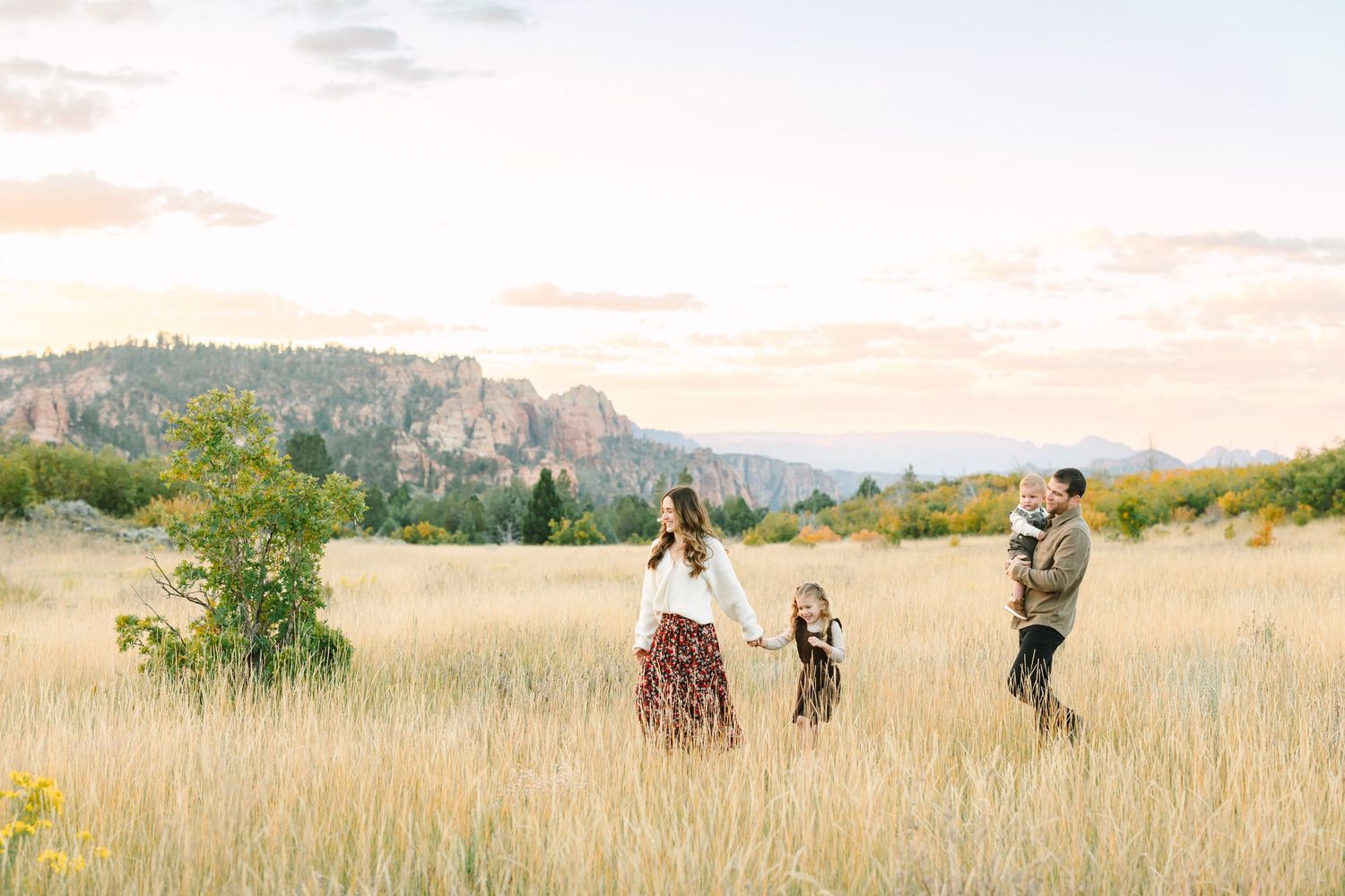 Photographers capturing scenic shots in a golden grassy field with mountains in the background during sunset.