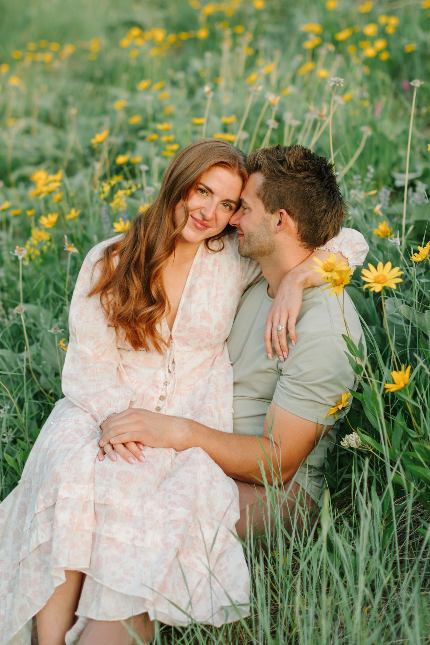 Couple sitting together in a field of yellow wildflowers during golden hour for their engagement photoshoot in Salt Lake City, Utah in Utah.