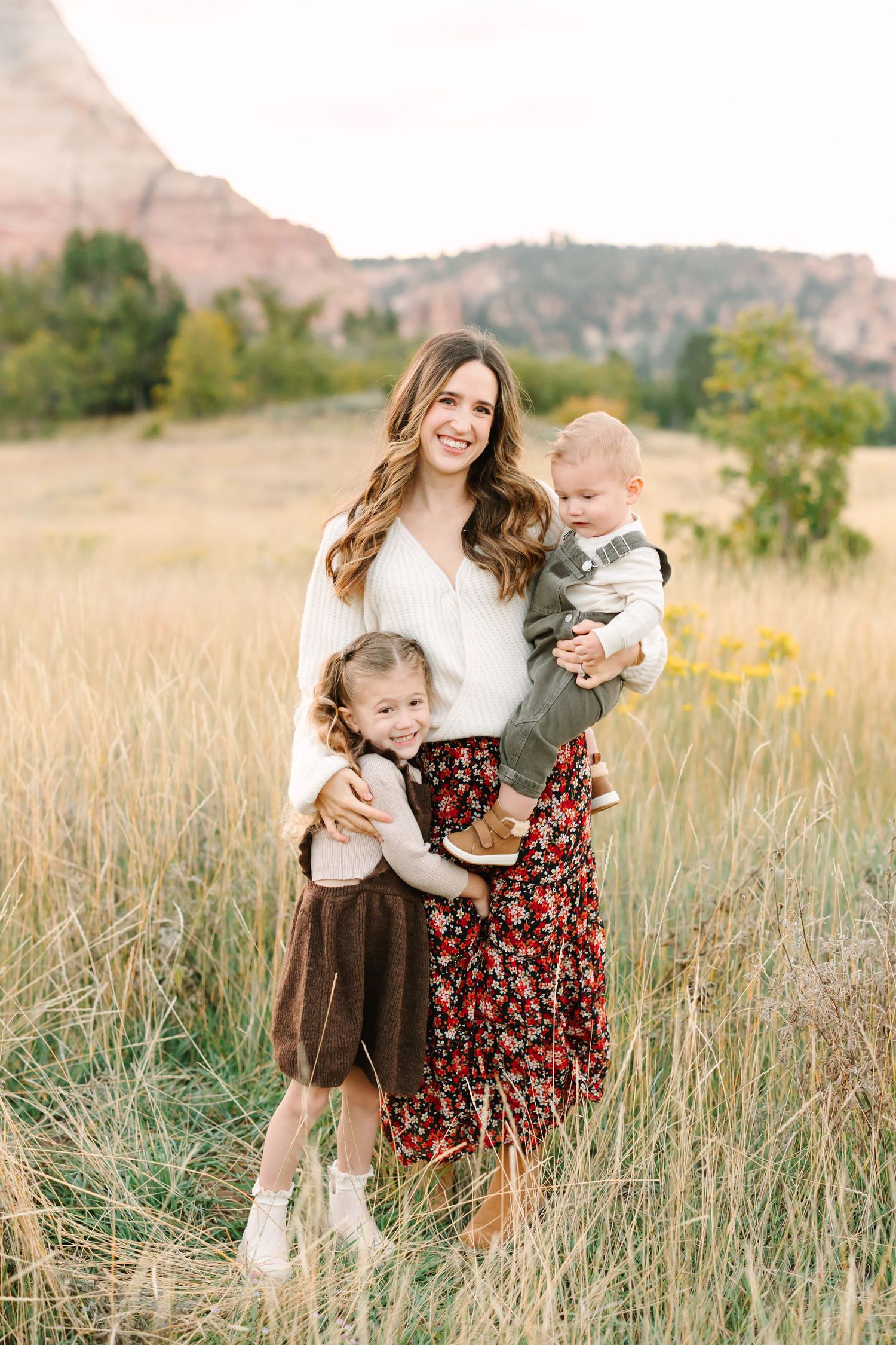 A family shares tender moments together in a golden wheat field during sunset with mountains in the background.