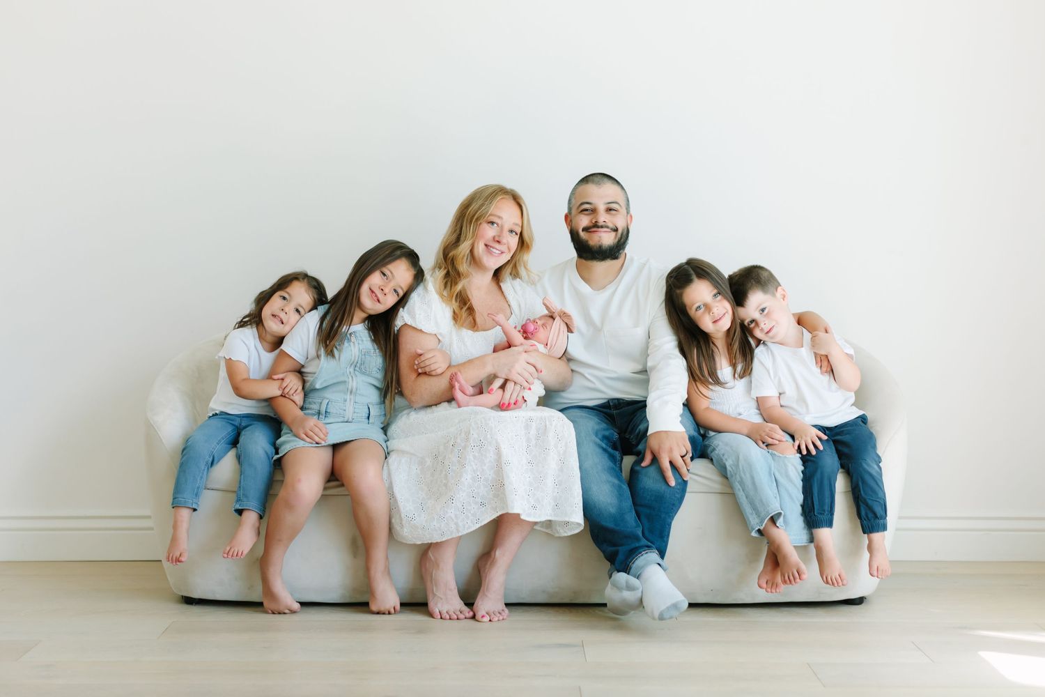 A family in coordinating blue and white outfits sits together on a white couch in a minimalist room.