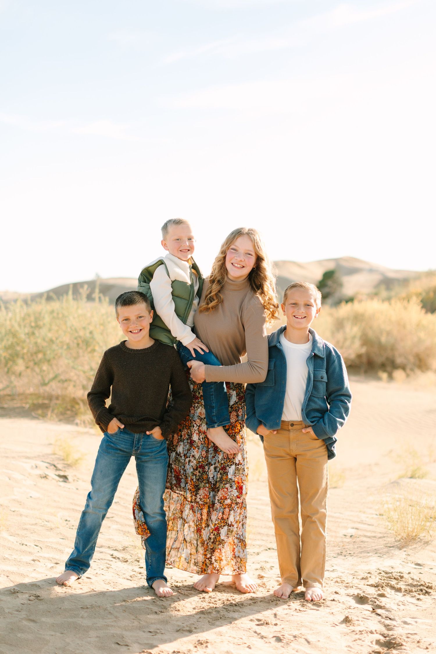 A family of four poses together outdoors on a sunny day in a desert landscape with mountains in the background.