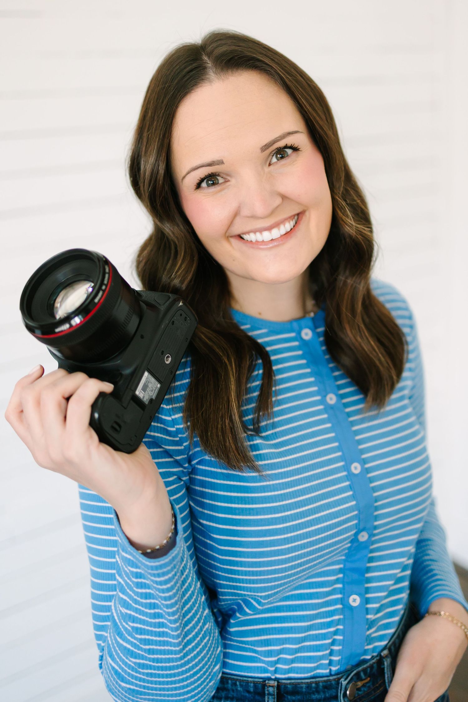 Professional photographer in blue striped shirt holding DSLR camera against white background in Utah County