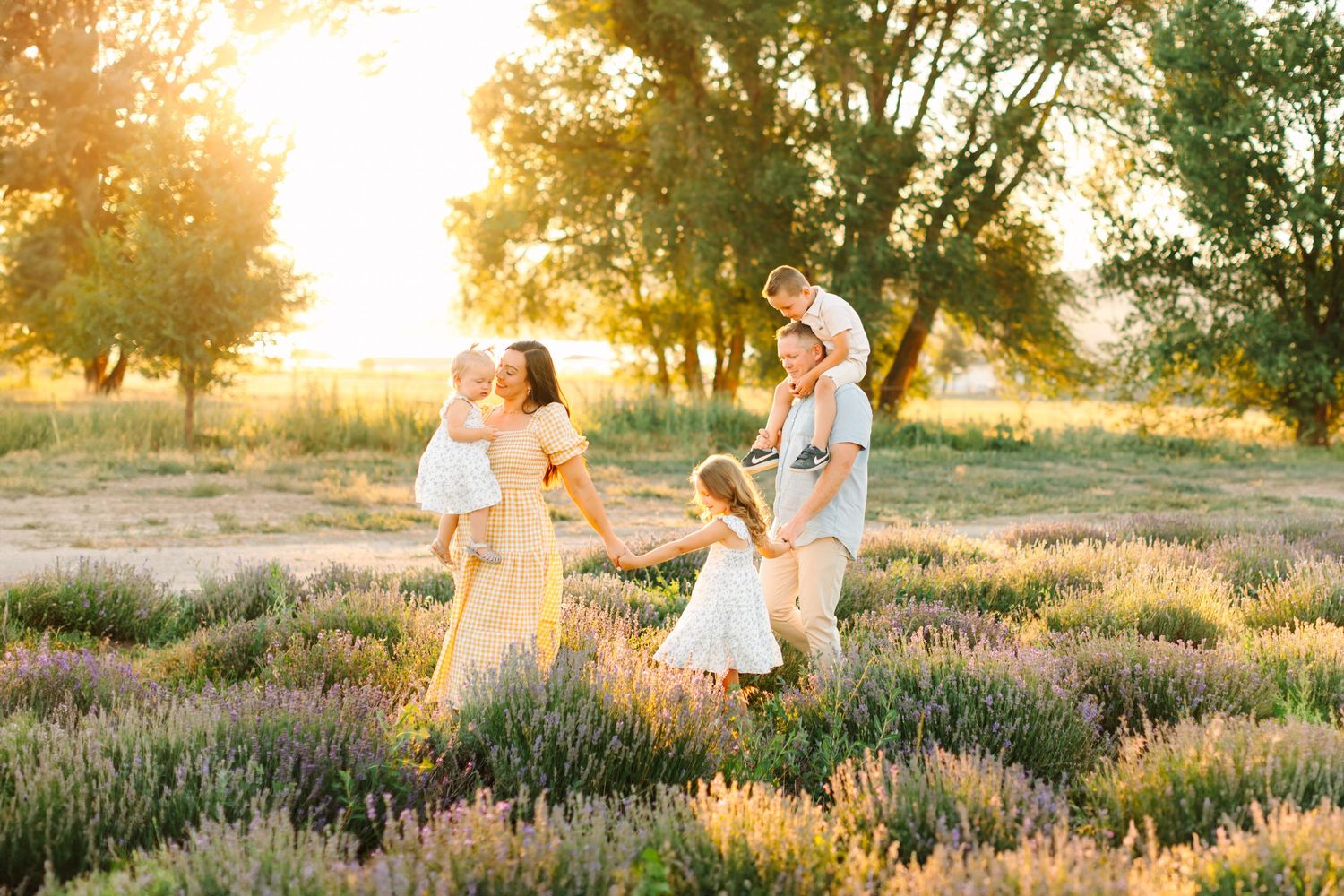 A family is walking hand in hand through purple lavender during golden hour at their family photoshoot in Mona, Utah.