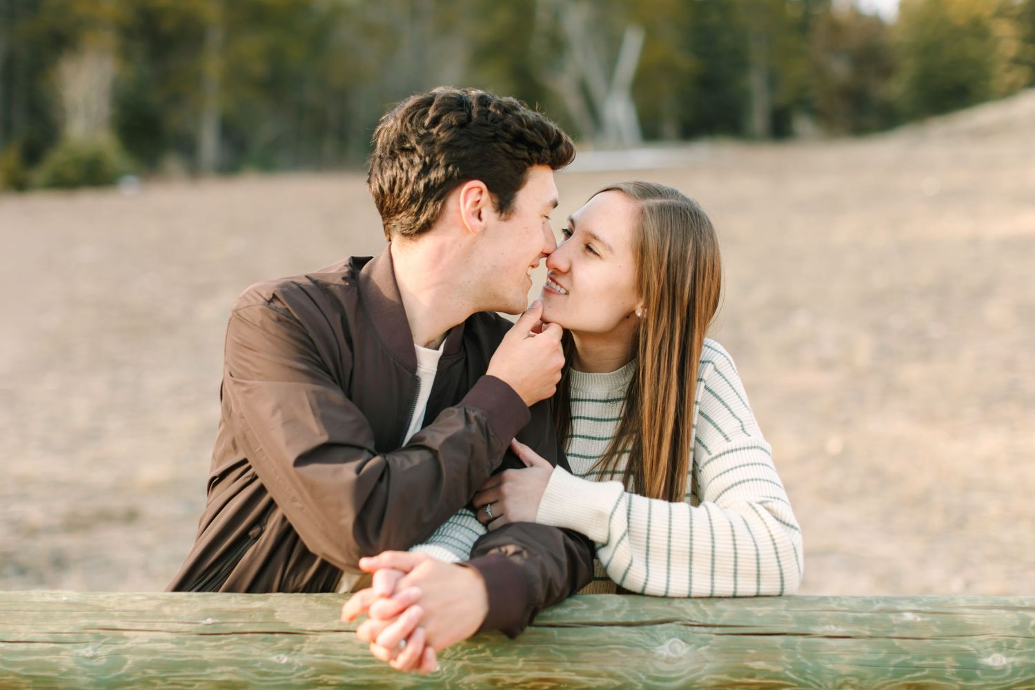 Couple sharing romantic kisses while laying on wooden deck during autumn sunset.
