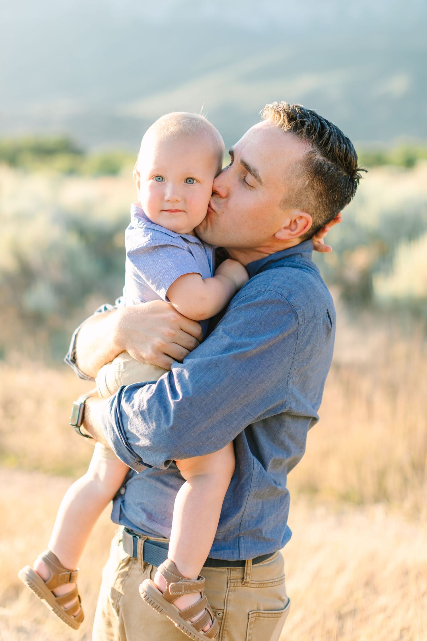 A tender moment captured in a golden field as a parent embraces and kisses their young child at sunset.