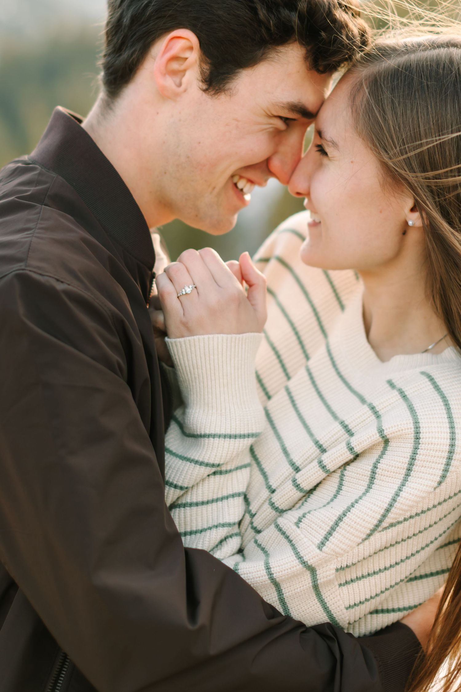 A romantic couple in a black sweater and striped scarf share an intimate moment during a golden hour photoshoot.