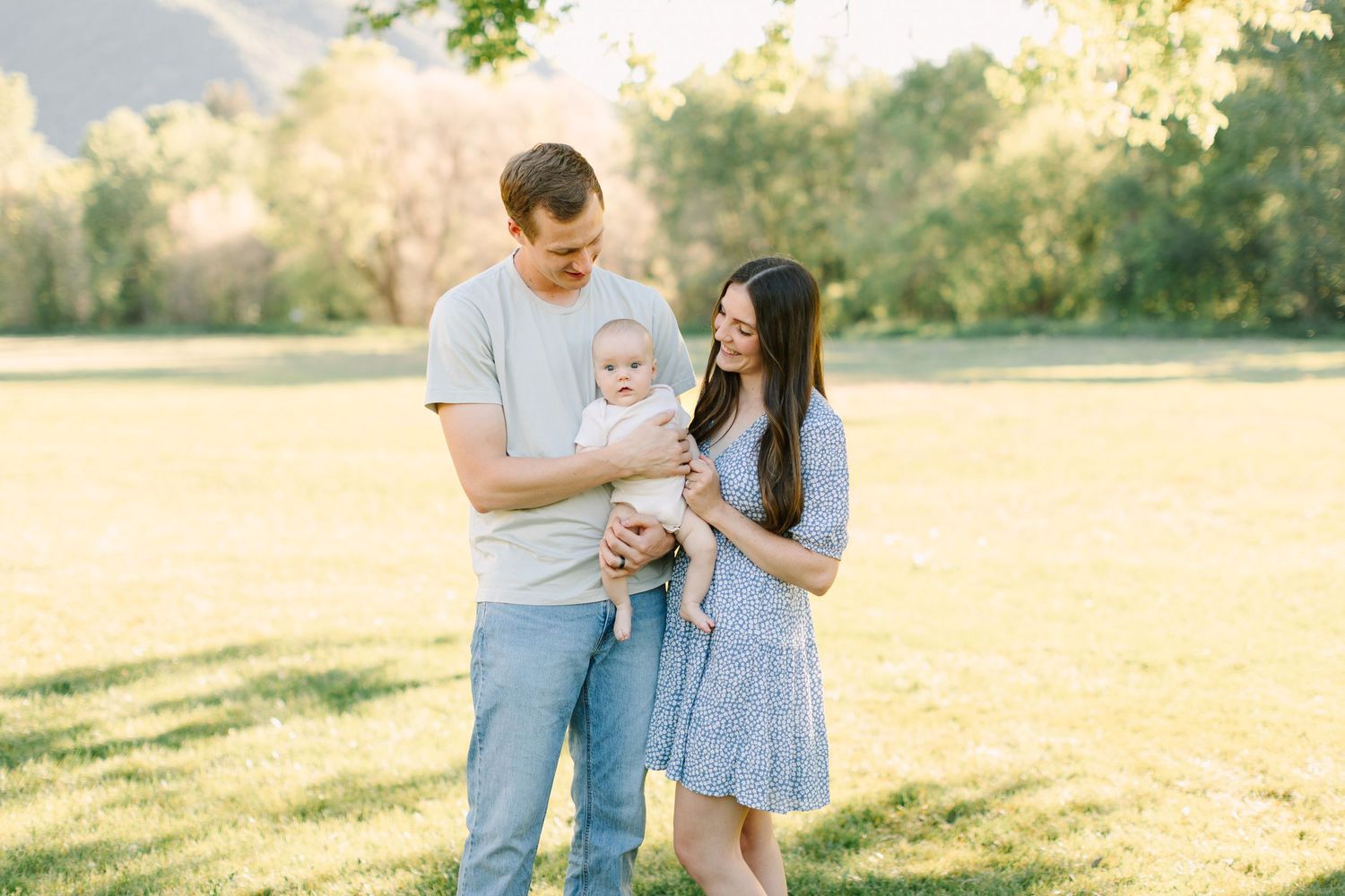 A couple in casual attire shares tender moments while walking together in a sunlit meadow during golden hour.