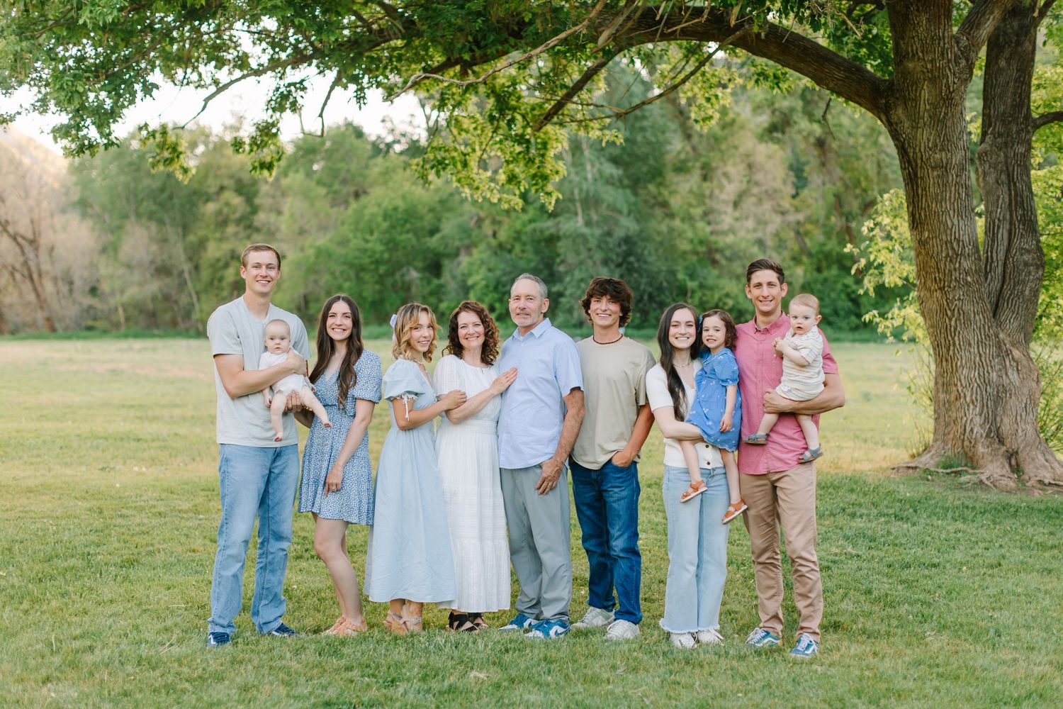 A group of people in coordinated pastel and denim outfits pose together outdoors in a grassy field at sunset.