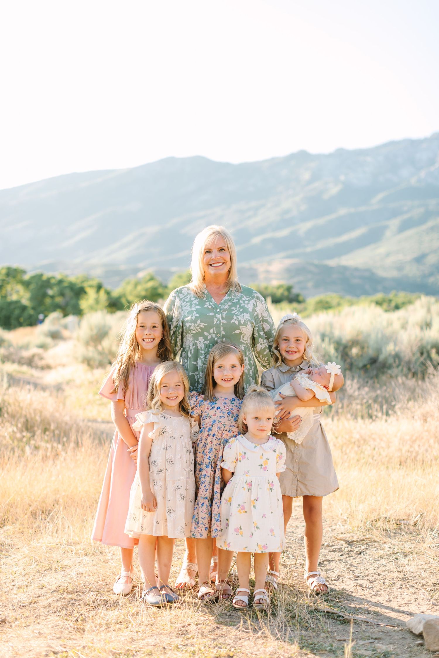 Family poses together in golden field with mountains in background during sunset photoshoot.